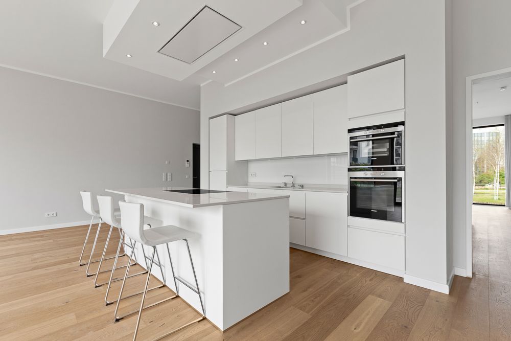 Moderne weiße Einbauküche mit Kochinsel und vier Barhockern auf Holzfußboden.