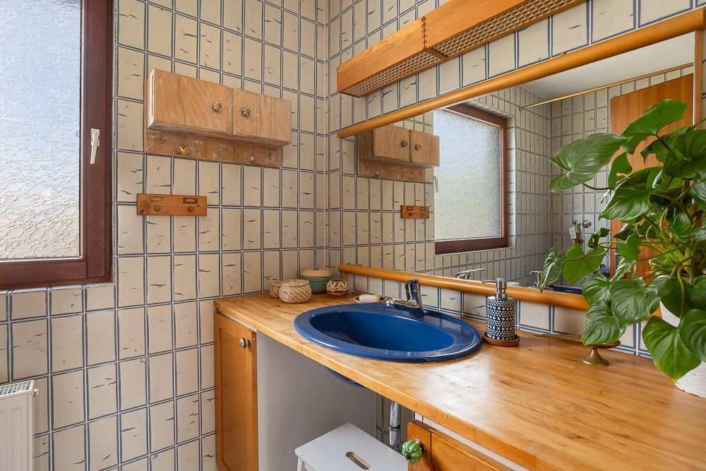 Badezimmer mit Holzwaschtisch, blauem Waschbecken, großem Spiegel und Pflanze.