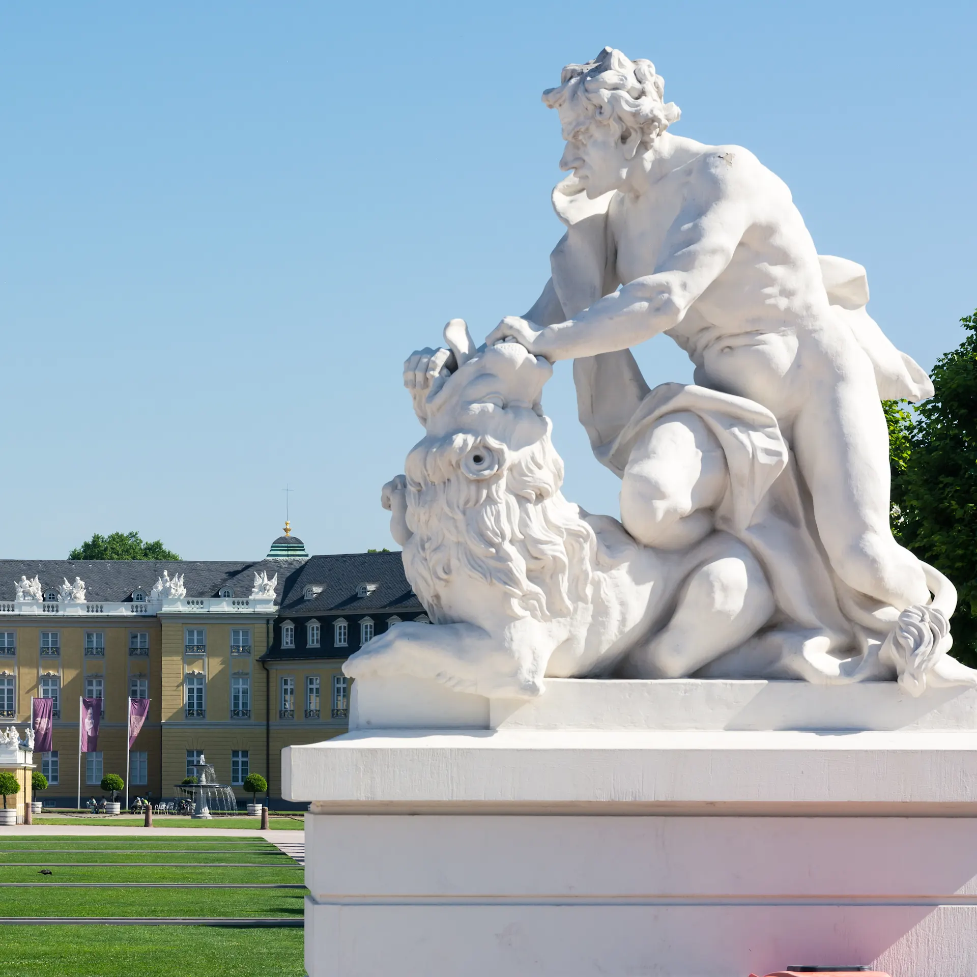 Großes gelbes Gebäude mit Turm und Statue eines Mannes mit Löwen im Vordergrund.