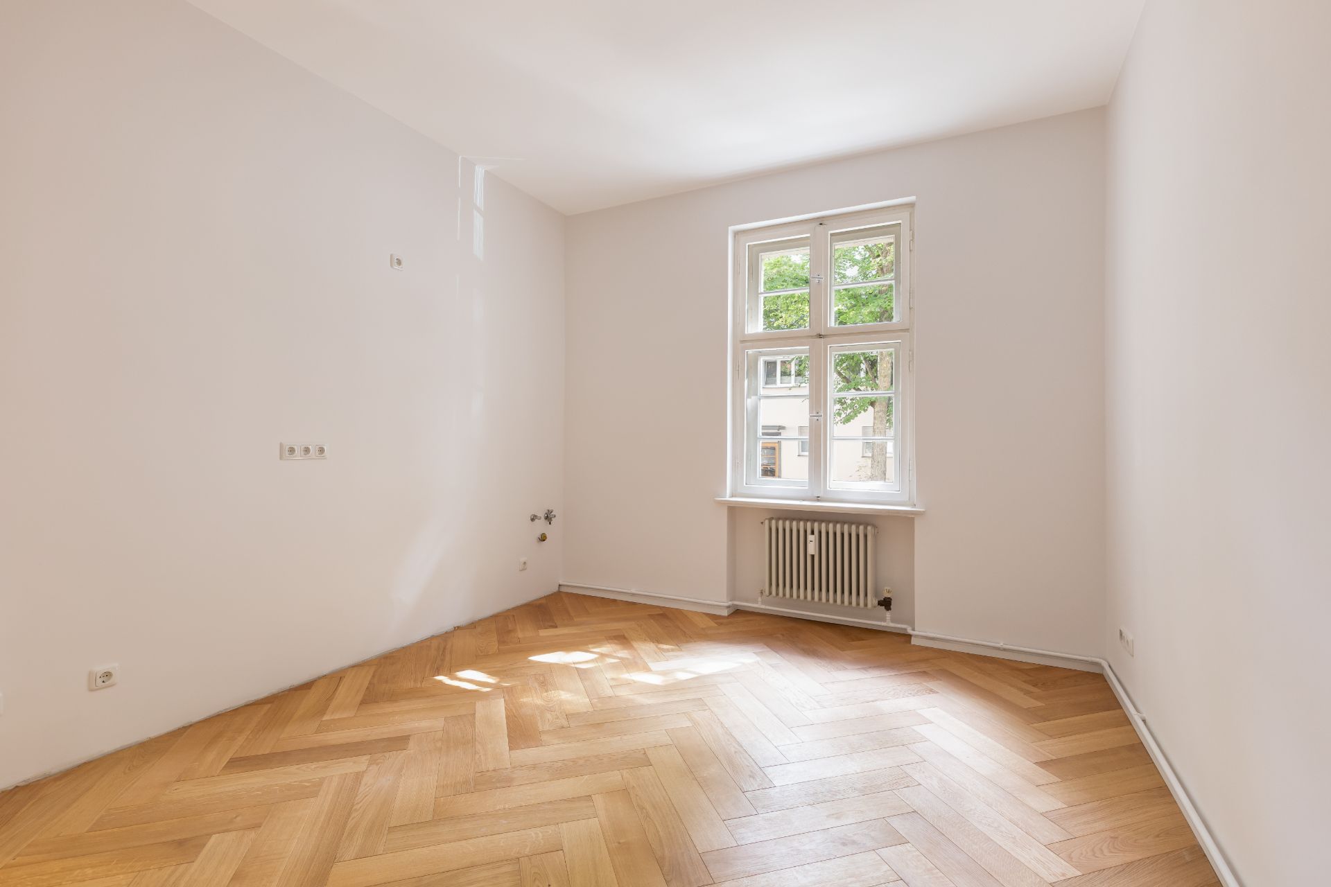 Heller, leerer Raum mit Parkettboden und Fenster mit Blick ins Grüne.