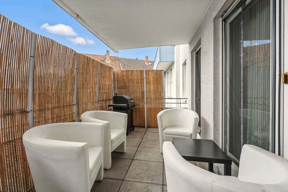 Balkon mit vier weißen Sesseln, einem schwarzen Tisch und einem Grill, umgeben von Bambusmatten.