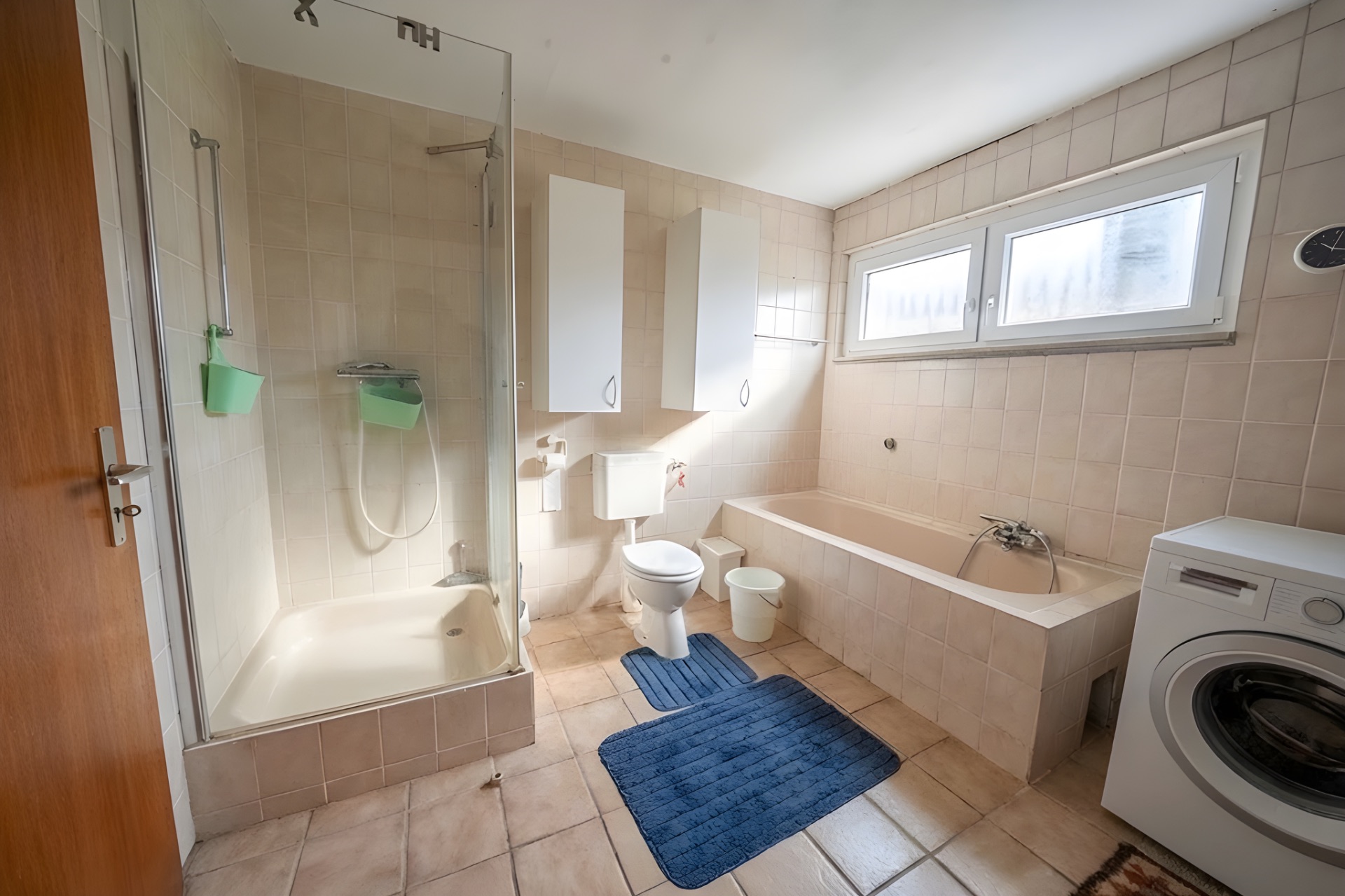 Badezimmer mit Dusche, Badewanne, Waschmaschine, Toilette und zwei blauen Badematten.