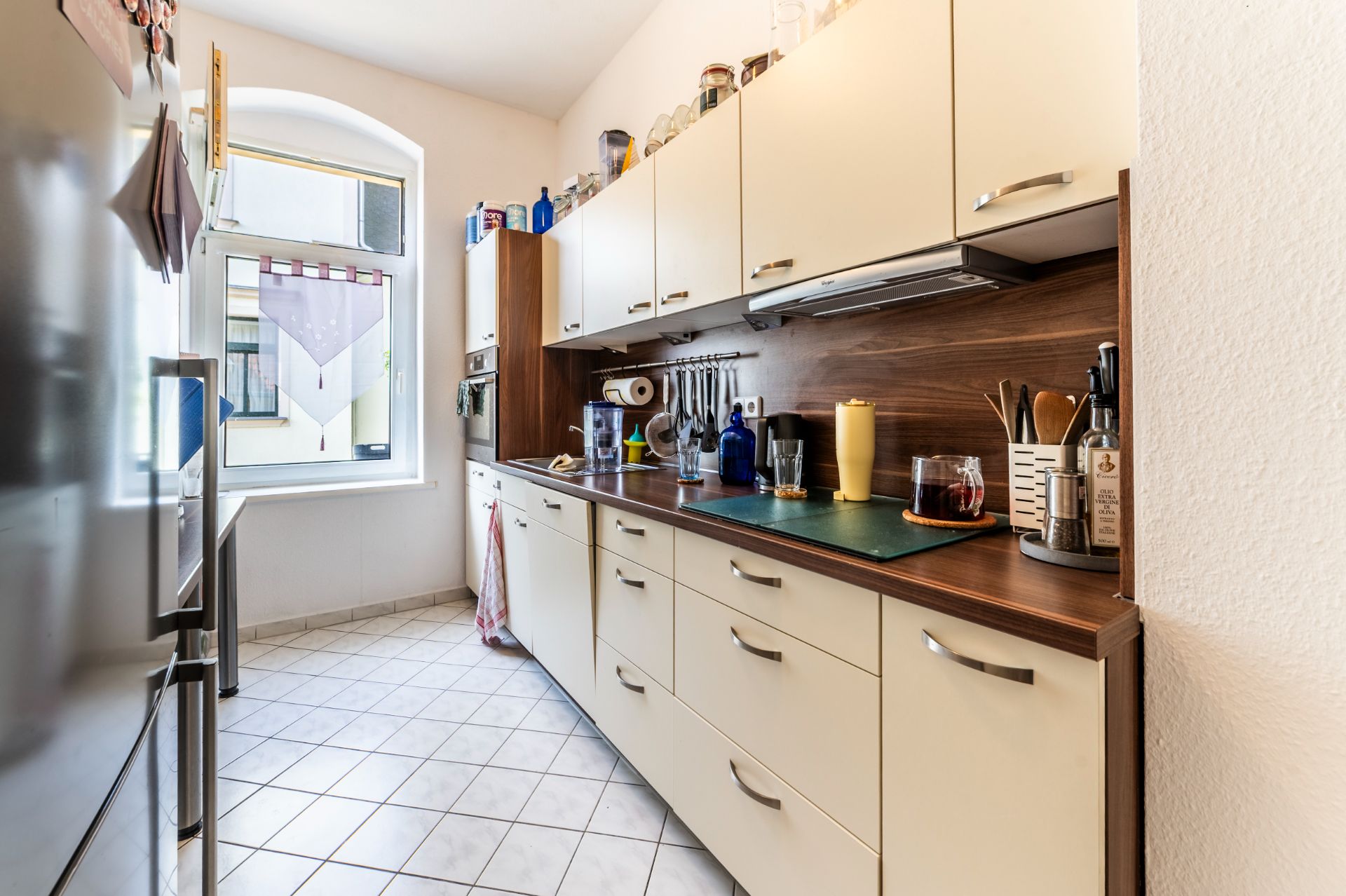 Schmale Küche mit weißen Schränken, Holzakzenten und Fenster am Ende des Raums.