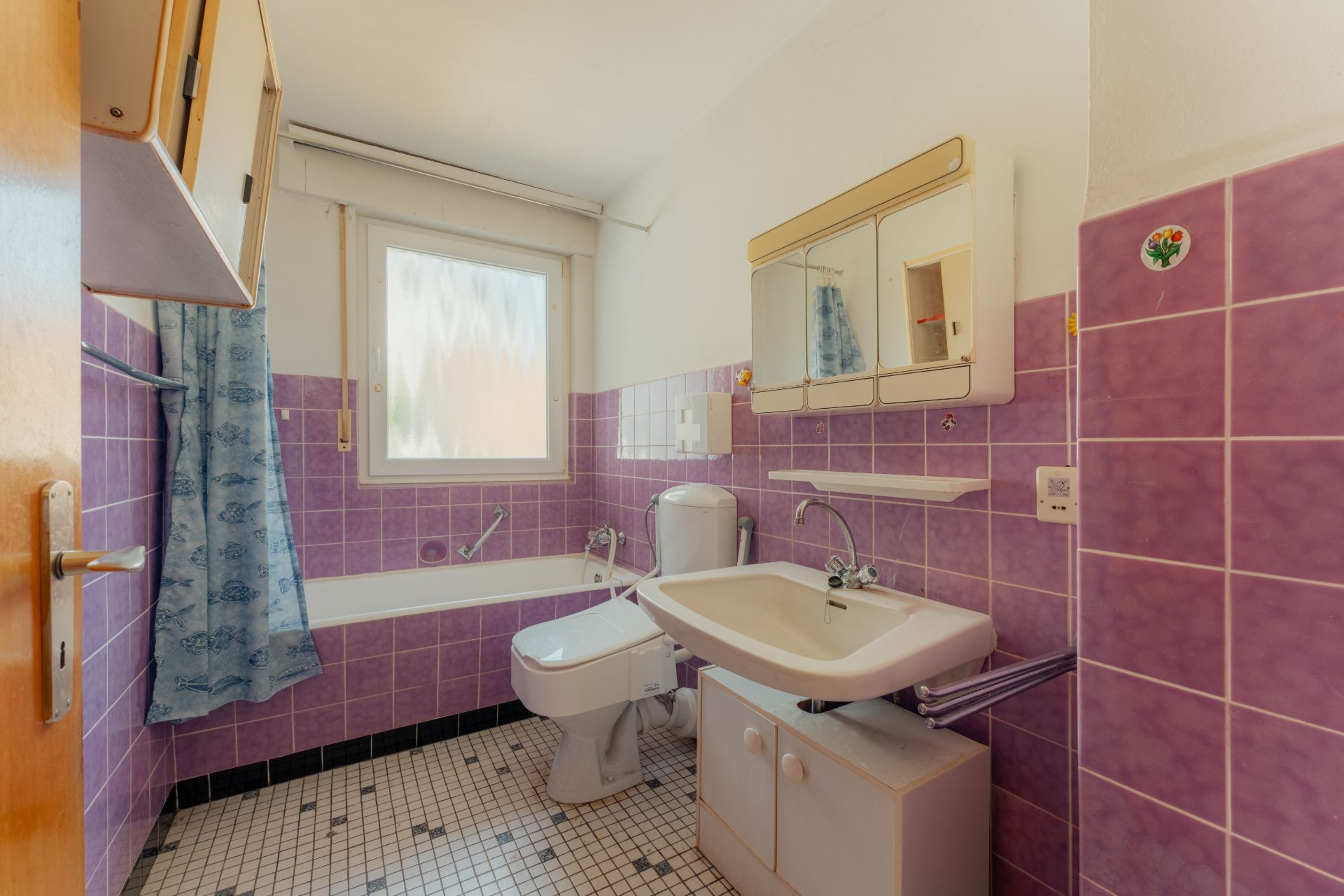 Badezimmer mit lila Fliesen, Badewanne, Toilette und Waschbecken mit Spiegel.
