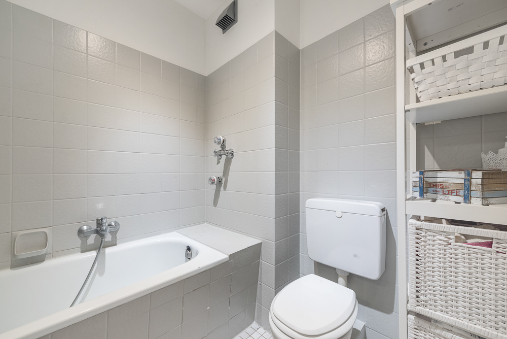 Helles Badezimmer mit Badewanne, Toilette und Regal mit Körben.