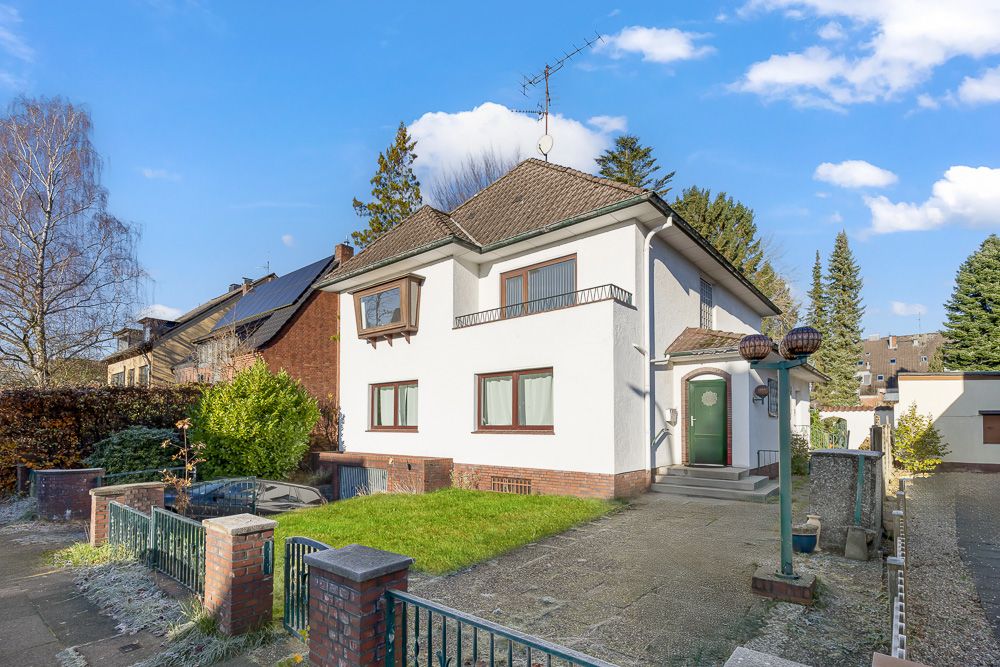 Zweistöckiges weißes Wohnhaus mit Garten, Einfahrt und grünem Tor im Vordergrund.