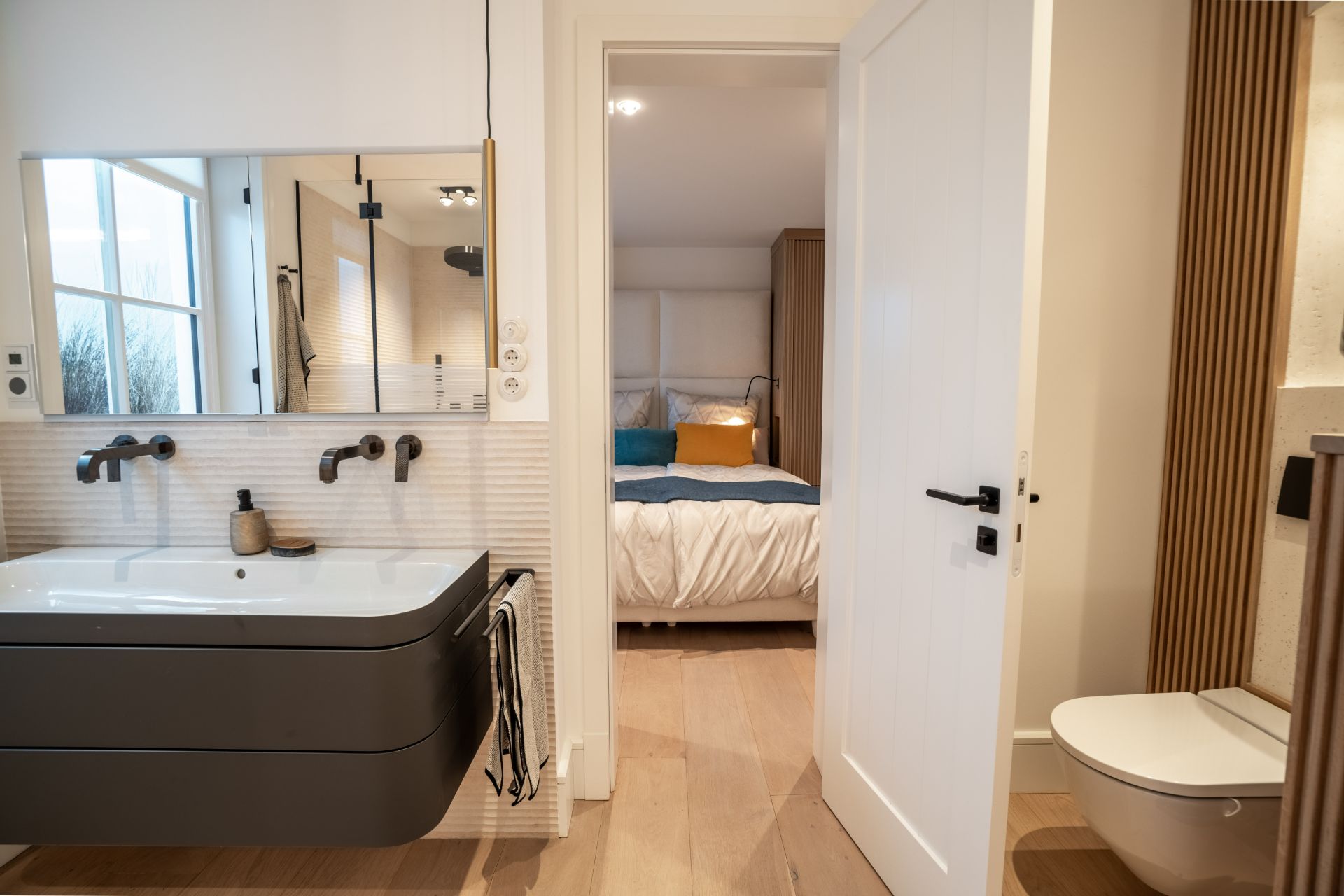 Modernes Badezimmer mit Waschtisch, Spiegel, WC und Blick ins Schlafzimmer.