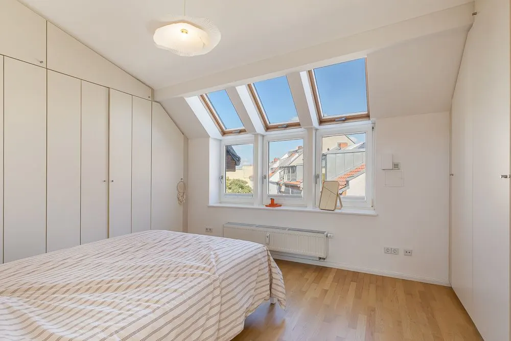 Helles Schlafzimmer mit Dachfenstern, Doppelbett, Holzboden und weißen Einbauschränken.