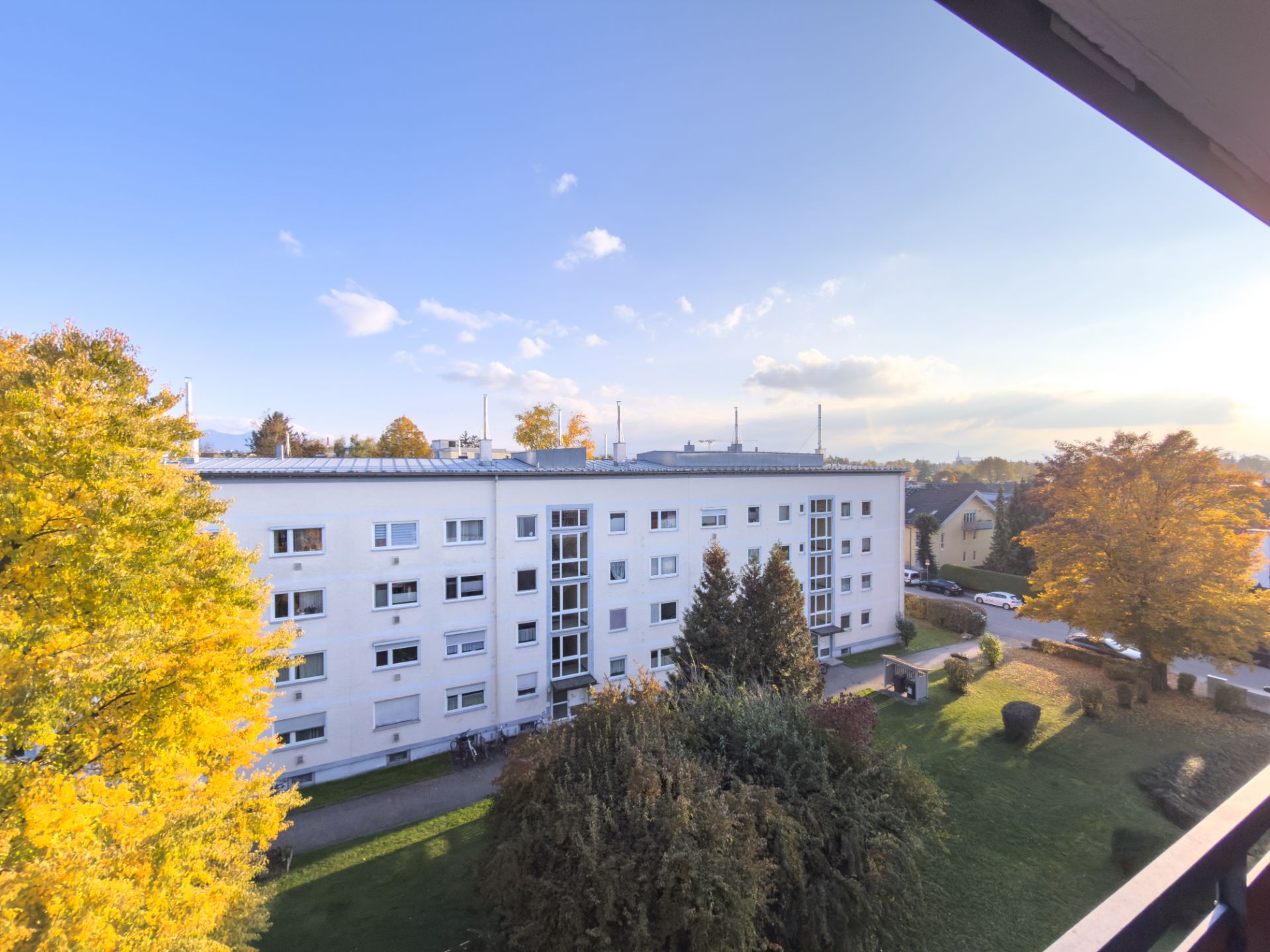 Mehrfamilienhaus mit mehreren Stockwerken und gepflegtem Garten, Bäume mit Herbstlaub.