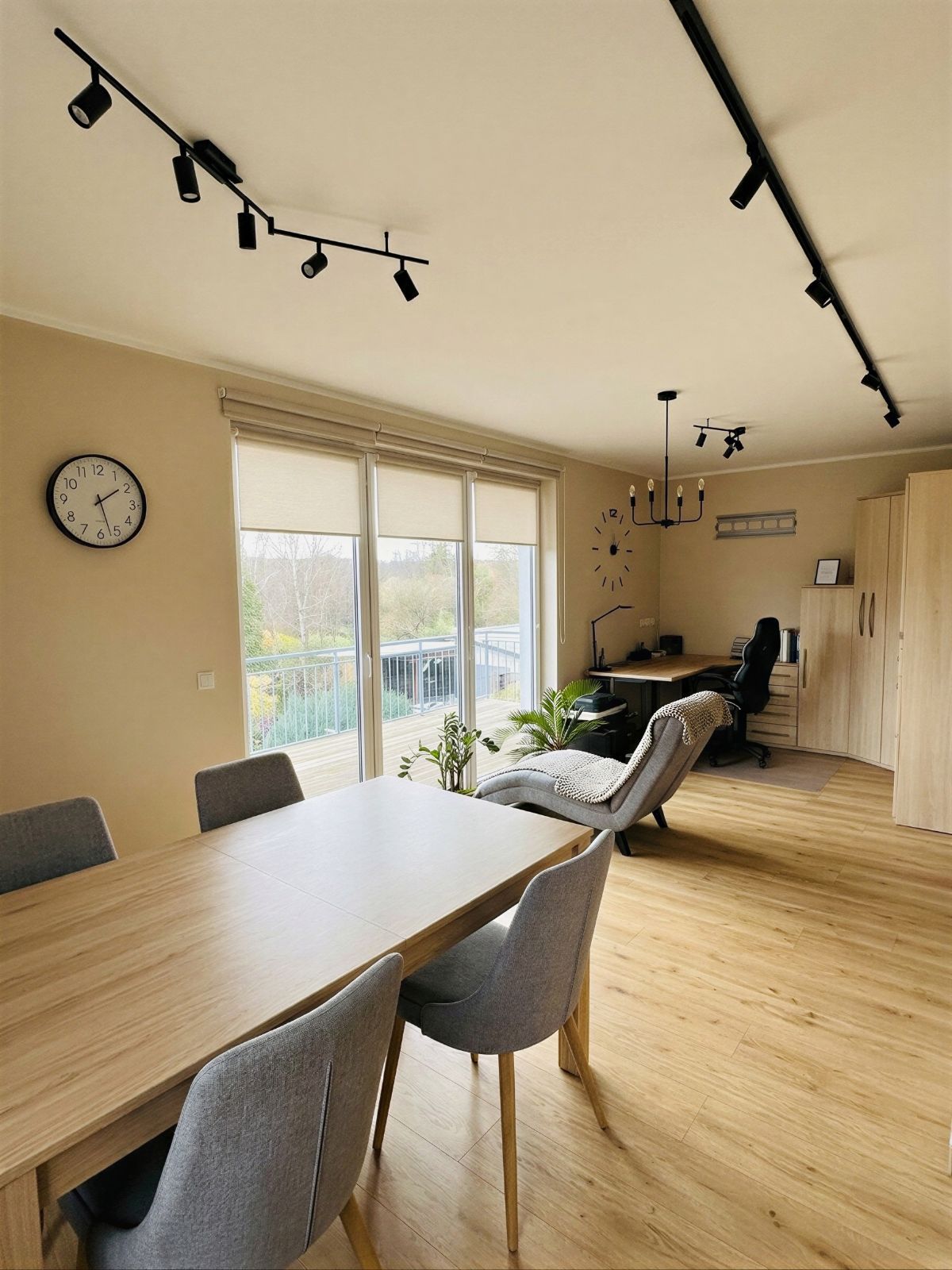 Helles Wohnzimmer mit Esstisch, Stühlen, Schreibtisch, Sessel und großen Fenstern.