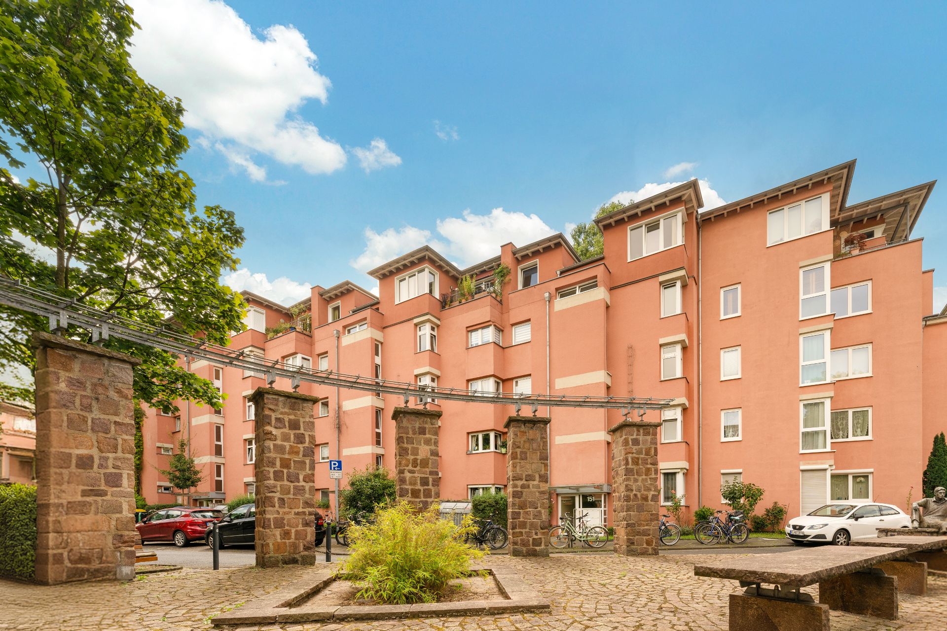 Mehrstöckiges Wohnhaus mit roten Fassaden, Steinpfeilern und parkenden Autos im Innenhof.