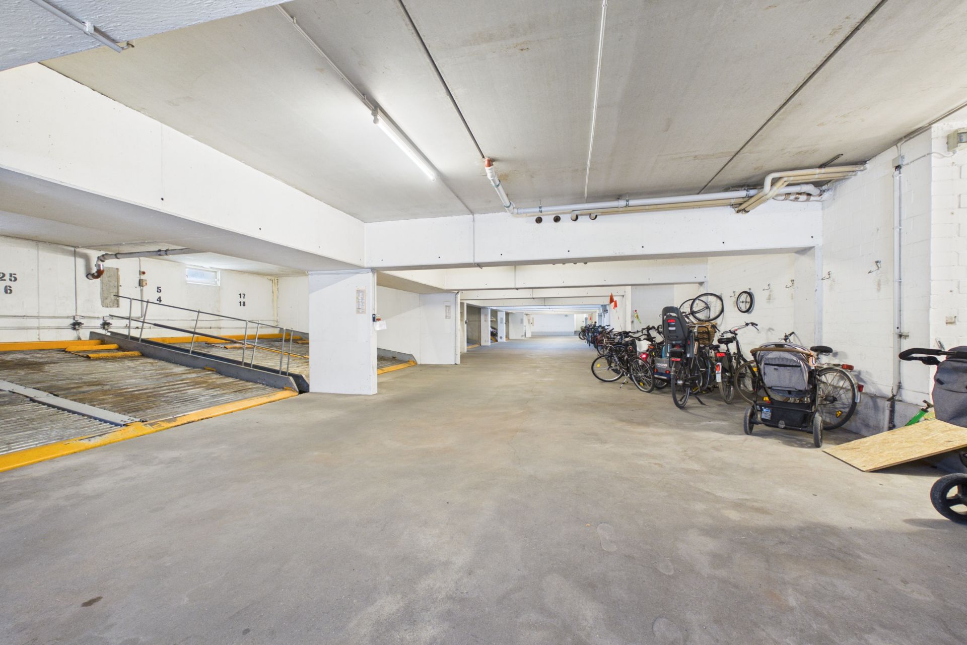 Helle Tiefgarage mit mehreren geparkten Fahrrädern und Fahrradanhängern an der rechten Wand.