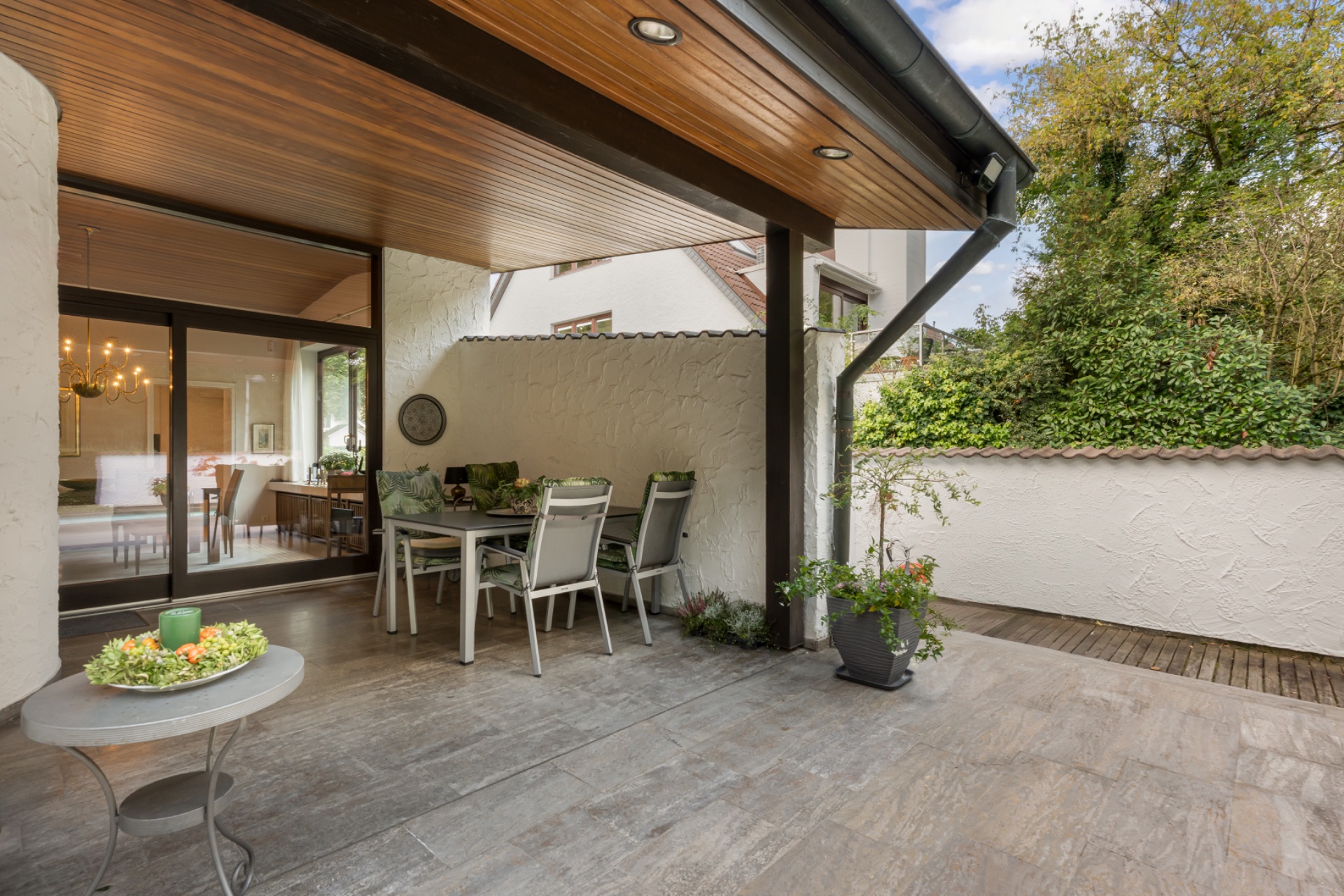 Überdachte Terrasse mit Esstisch und Stühlen, Blick auf Gartenmauer und Pflanzen.