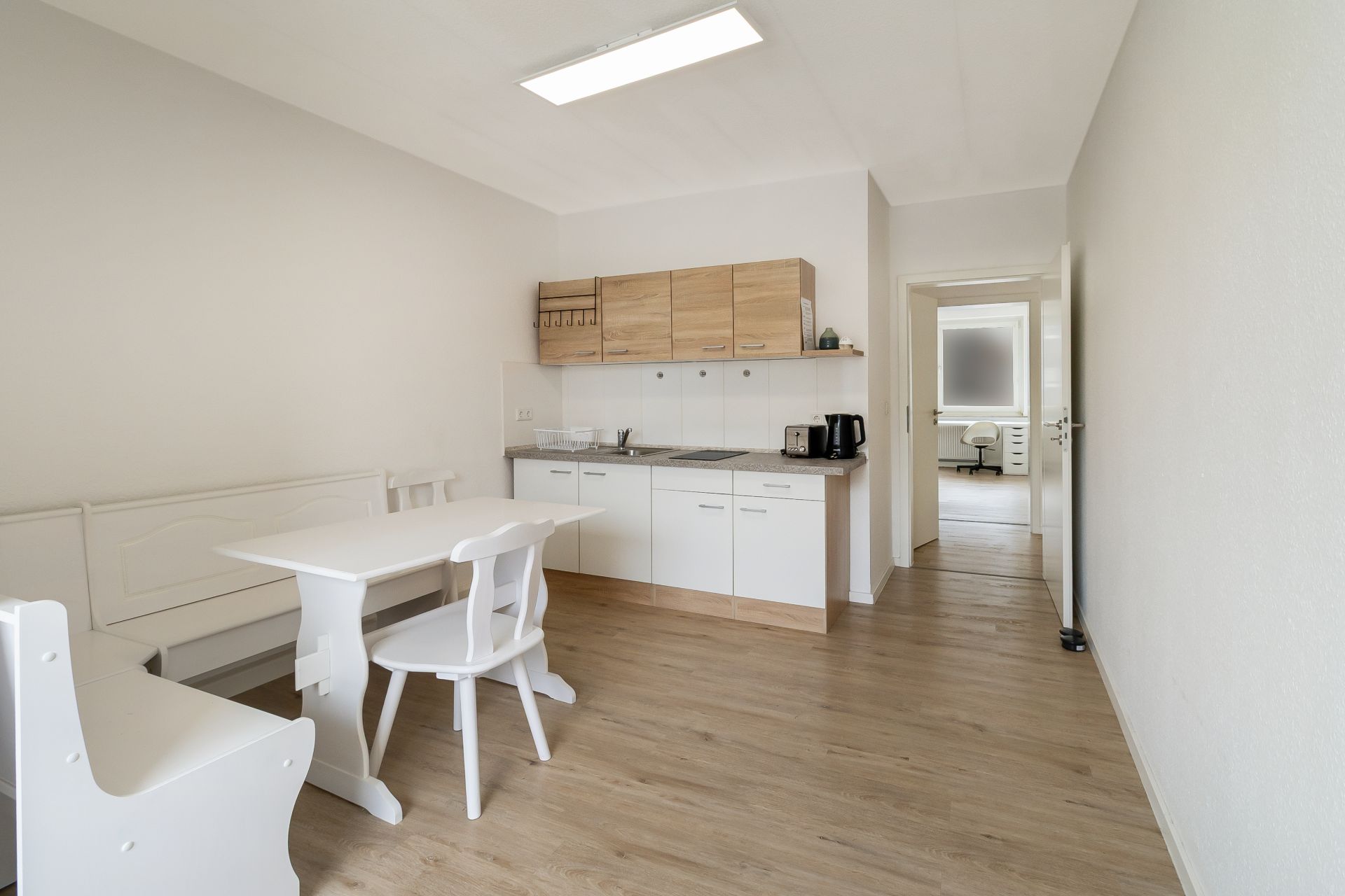 Helle Wohnküche mit Esstisch, weißen Stühlen und moderner Küchenzeile aus Holz.