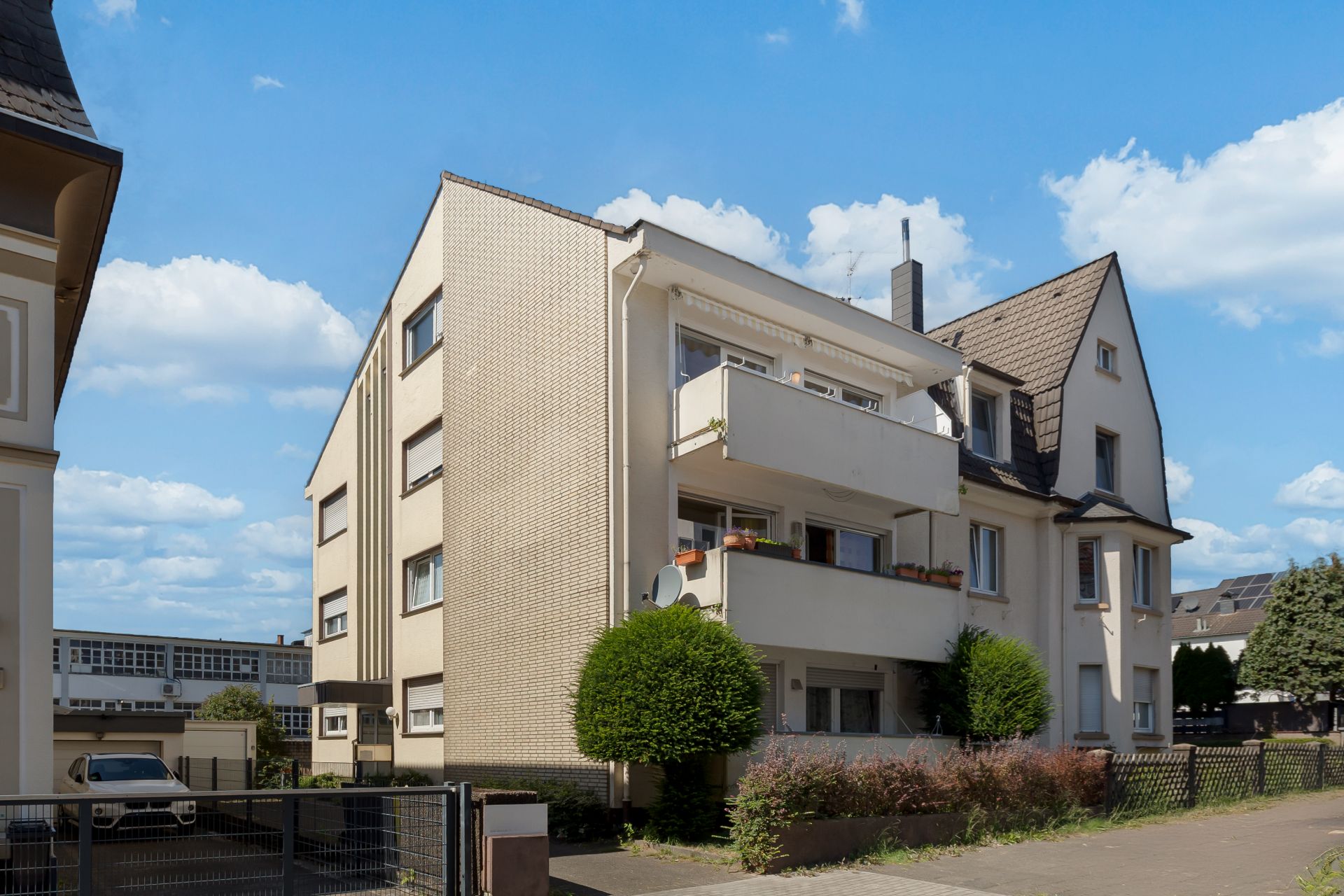 Mehrfamilienhaus mit Balkonen, gepflegten Büschen und Bäumen vor dem Gebäude.