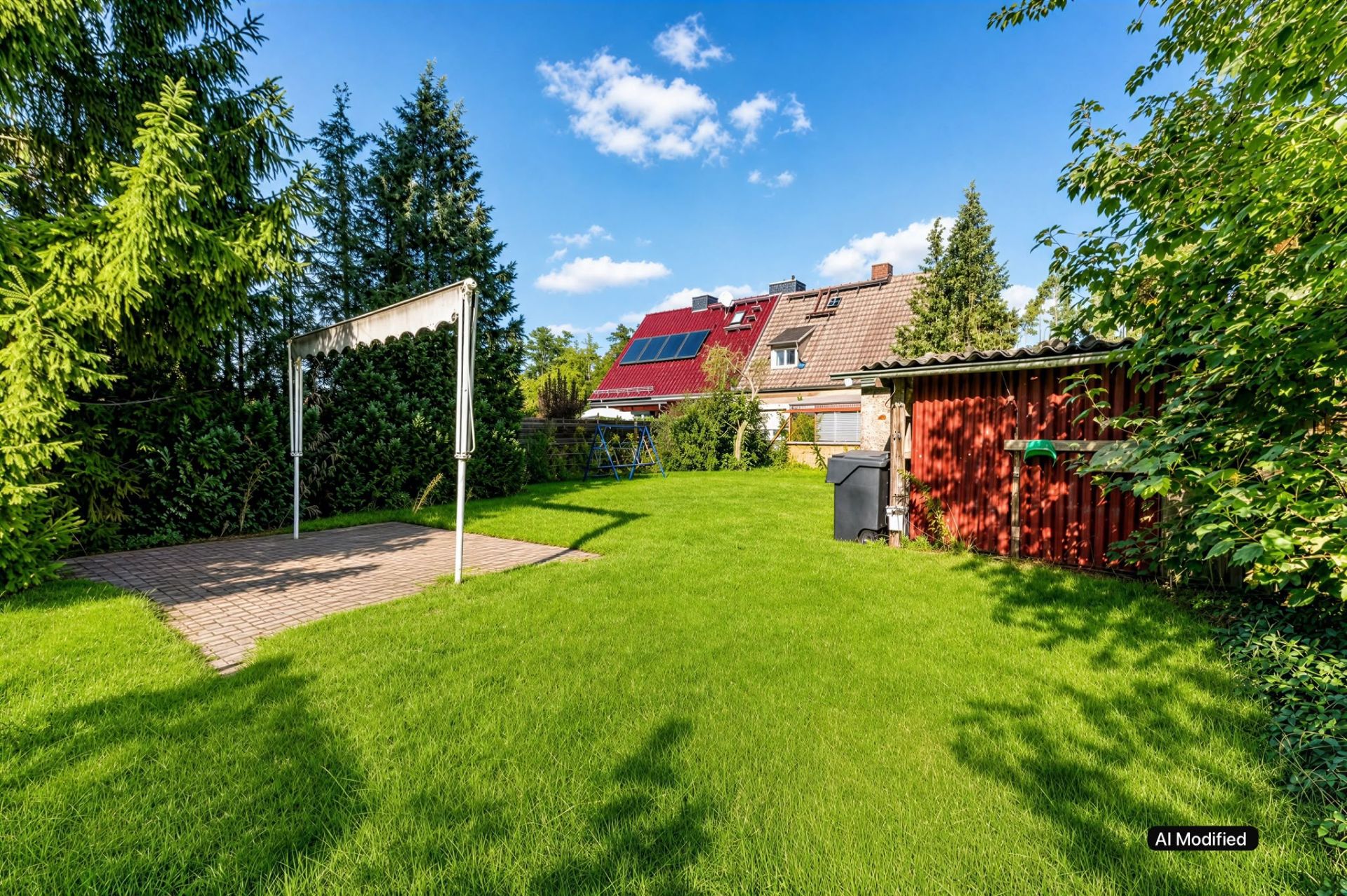 Grüner Garten mit Terrasse, Wäscheleine, rotem Schuppen und Bäumen unter blauem Himmel.