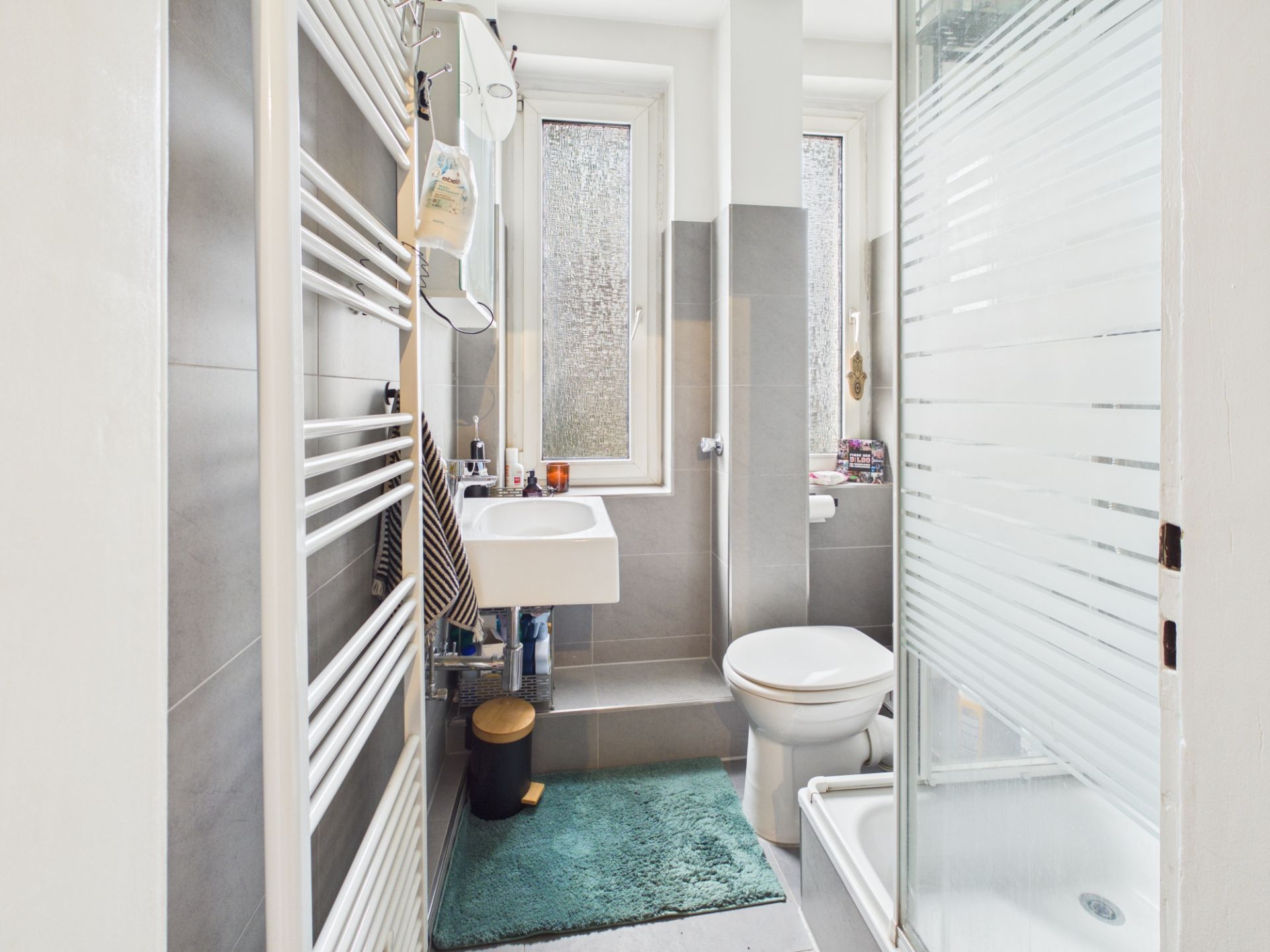 Modernes kleines Badezimmer mit Dusche, Waschbecken, Toilette und zwei Fenstern.