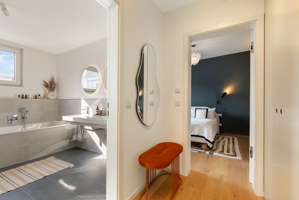 Flur mit Bank und Spiegel, links Badezimmer, rechts Schlafzimmer mit Teppich.