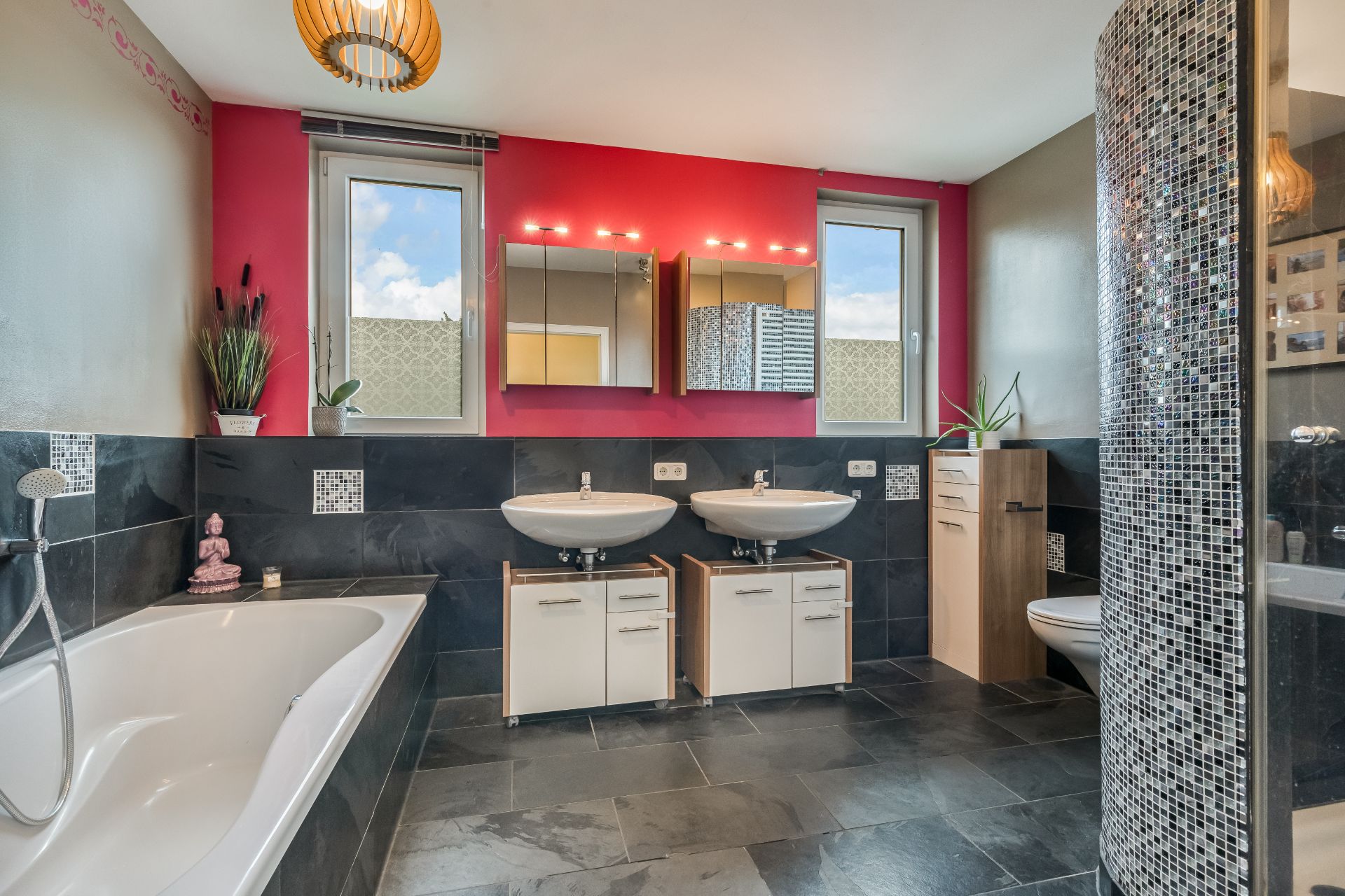 Modernes Badezimmer mit Badewanne, zwei Waschbecken, Spiegeln und schwarzen Fliesen.