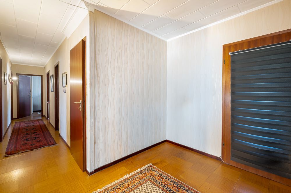 Heller Flur mit Holztüren, weißer Decke, Parkettboden und Teppichen.