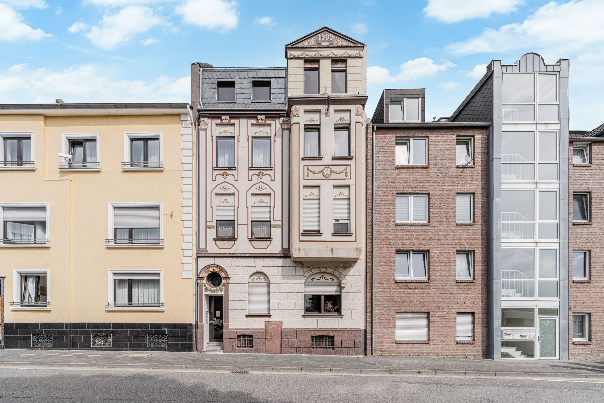 Mehrstöckiges Wohnhaus mit verzierten Fassadenelementen, Baujahr 1909, zwischen weiteren Wohngebäuden.
