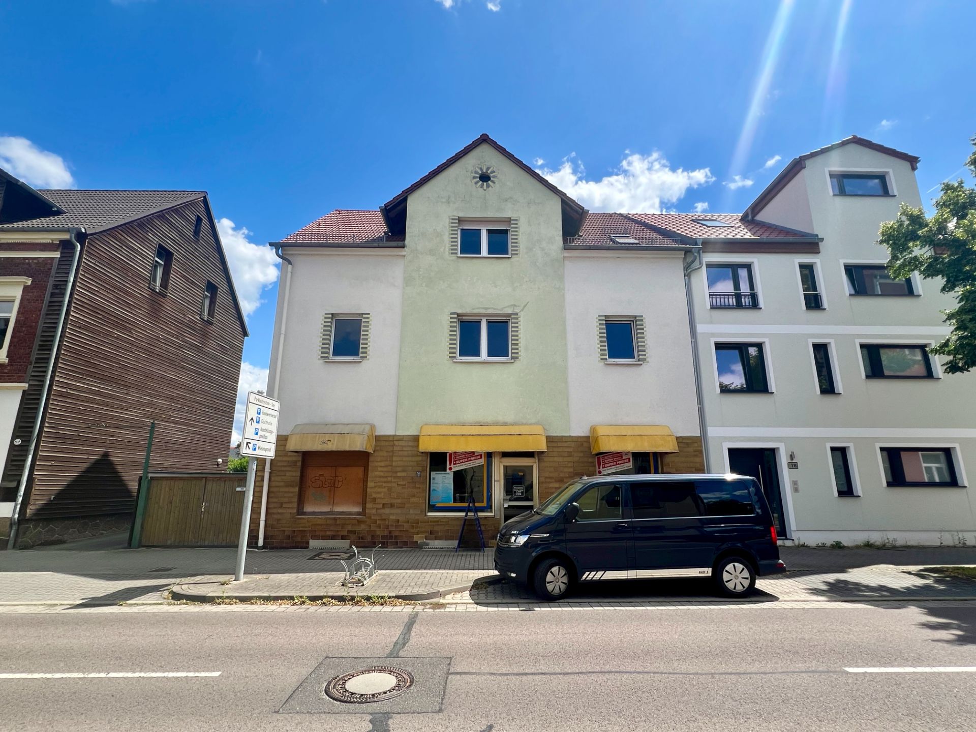 Dreistöckiges Wohnhaus mit gelben Markisen und geparktem schwarzen Van davor.