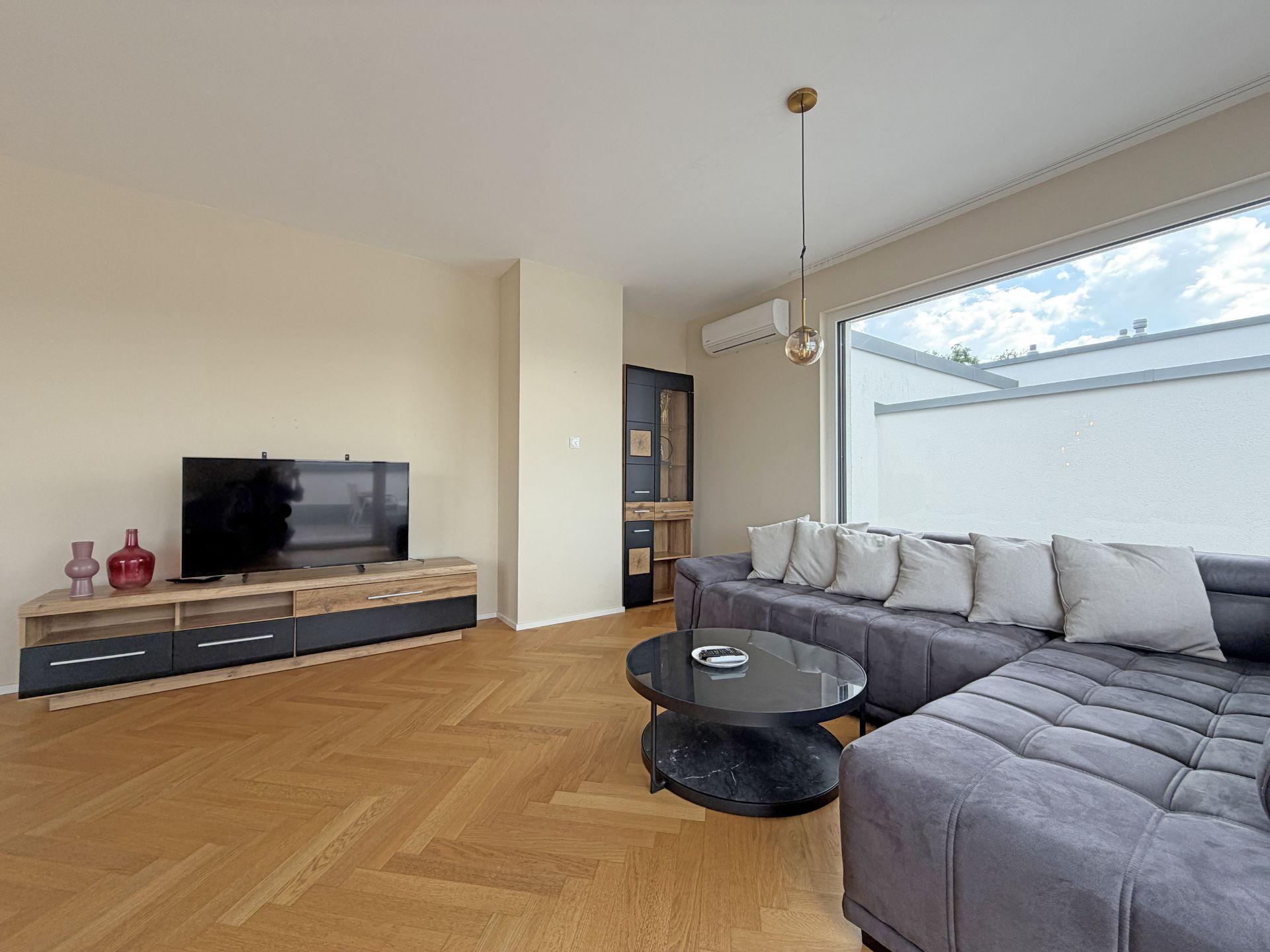 Modernes Wohnzimmer mit grauem Ecksofa, Couchtisch, TV und großem Fenster.