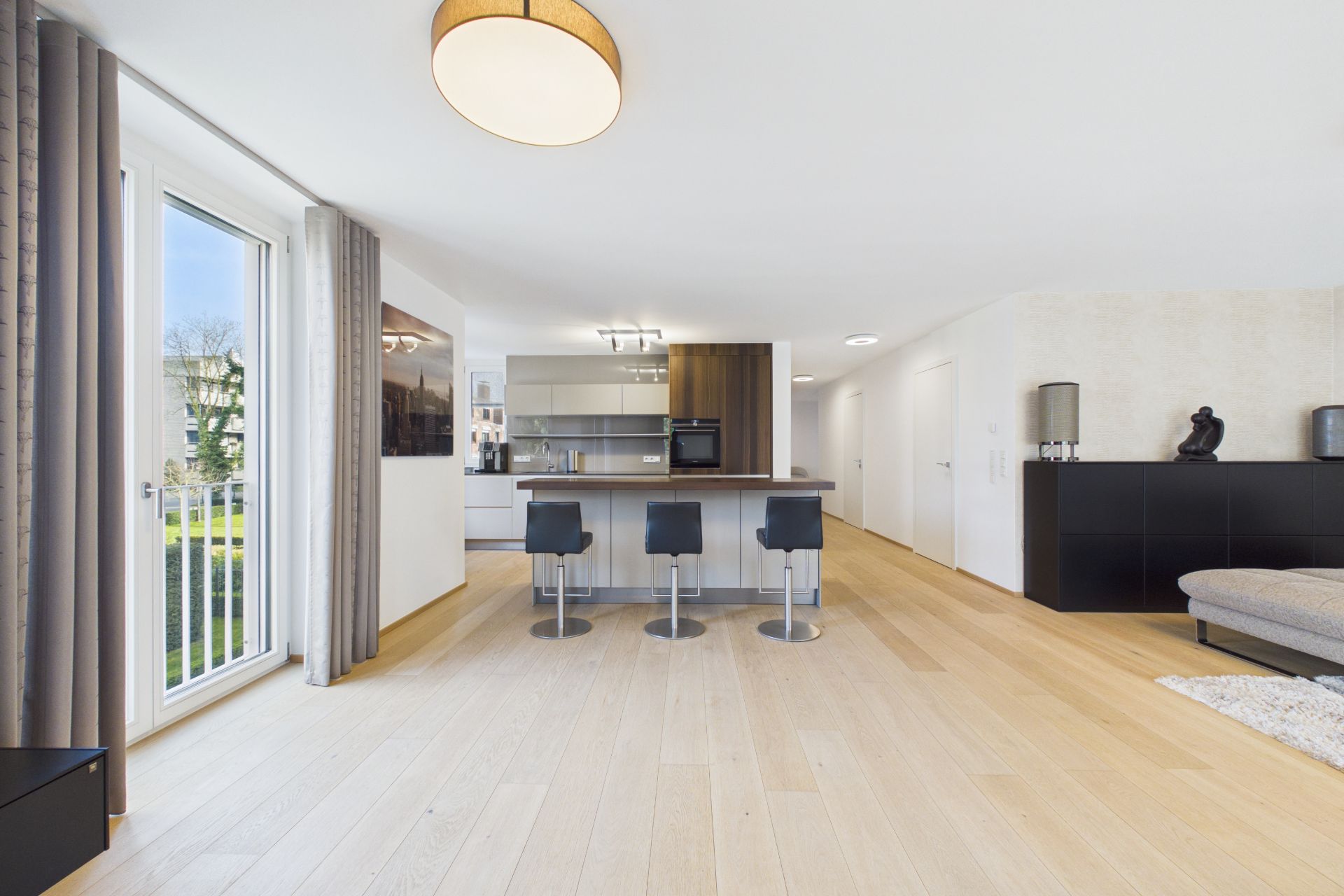 Helle Küche mit Kochinsel, drei Barhockern und offenem Wohnraum mit Holzfußboden.