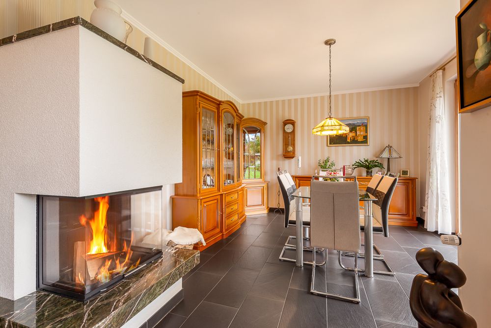 Esszimmer mit Glastisch, sechs Stühlen, Kamin und Holzvitrine, moderne Dekoration.