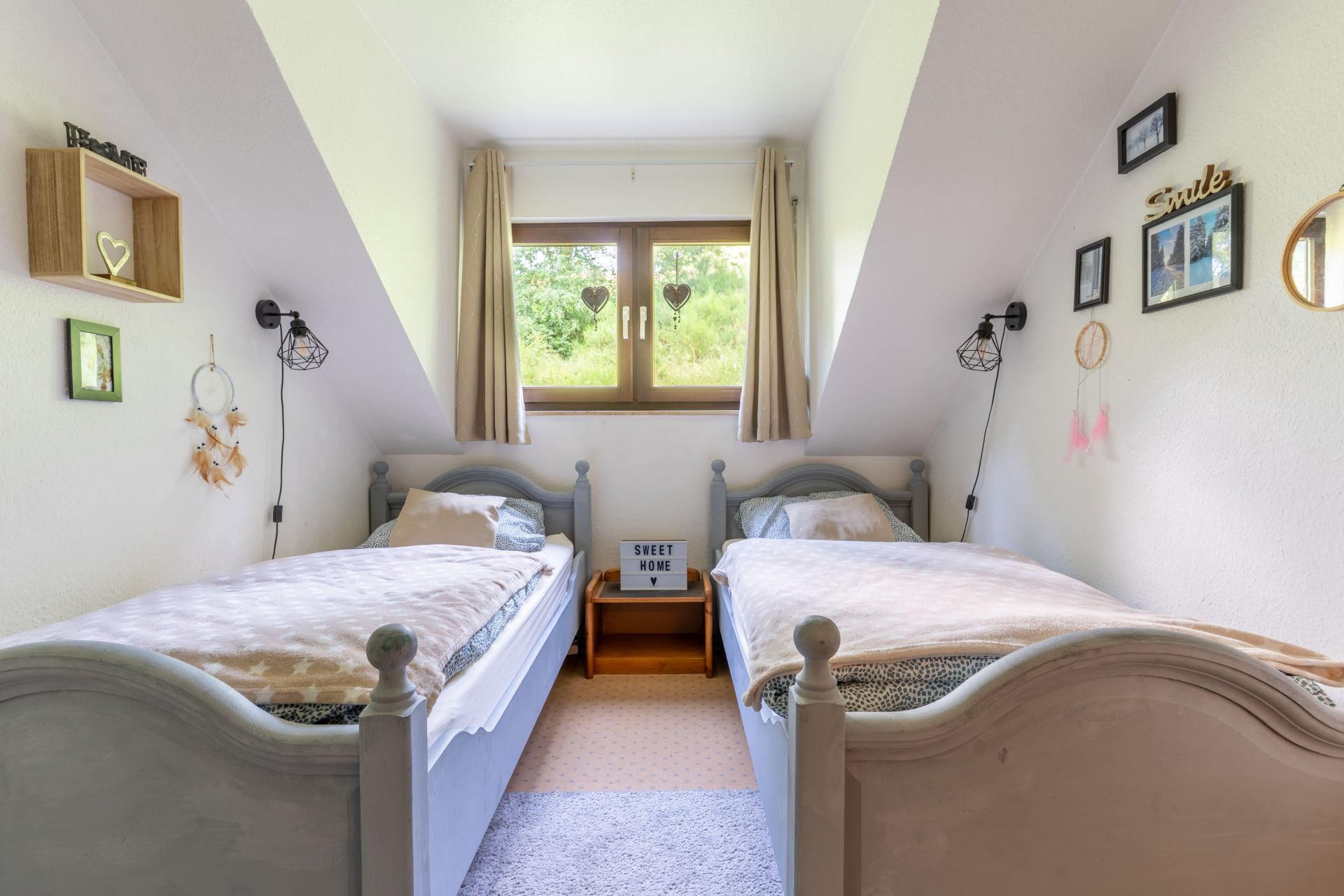Helles Schlafzimmer mit zwei Einzelbetten, Fenster mit Vorhängen und dekorierten Wänden.