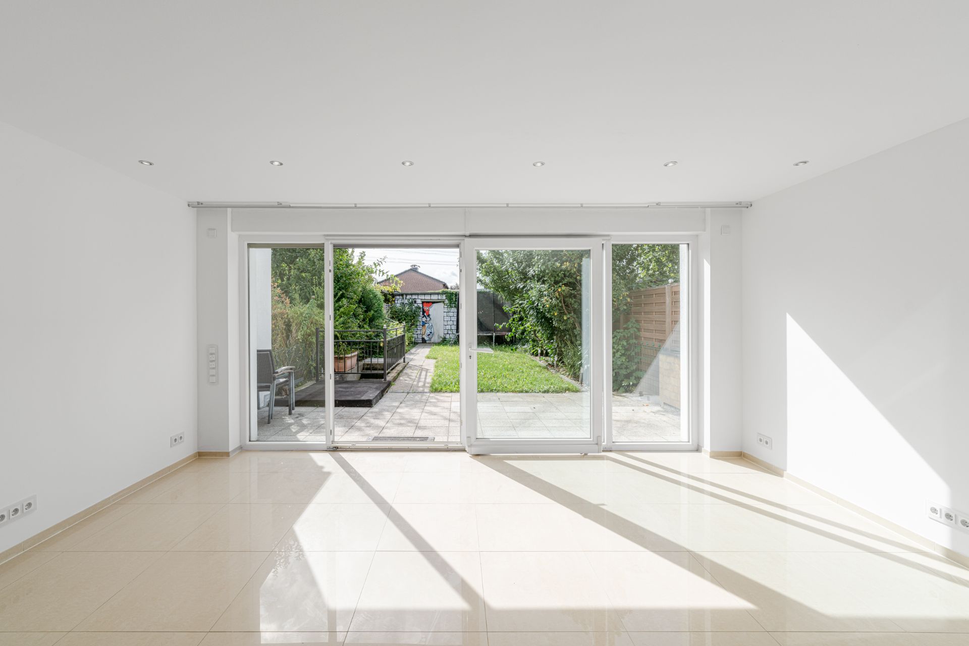 Helles, leeres Zimmer mit großen Glas-Schiebetüren zum Garten mit Terrasse und Rasen.