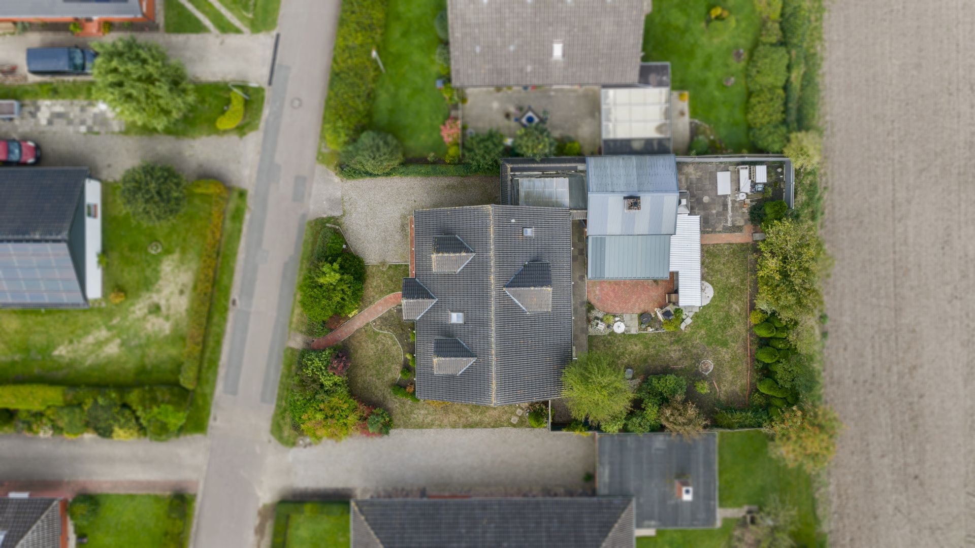 Luftaufnahme eines Hauses mit Garten, Auffahrt und Nachbargrundstücken.