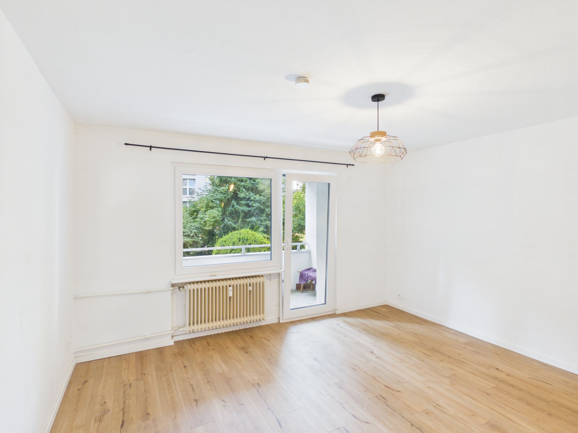 Helles leeres Zimmer mit Holzfußboden, Fenster und Tür zum Balkon.