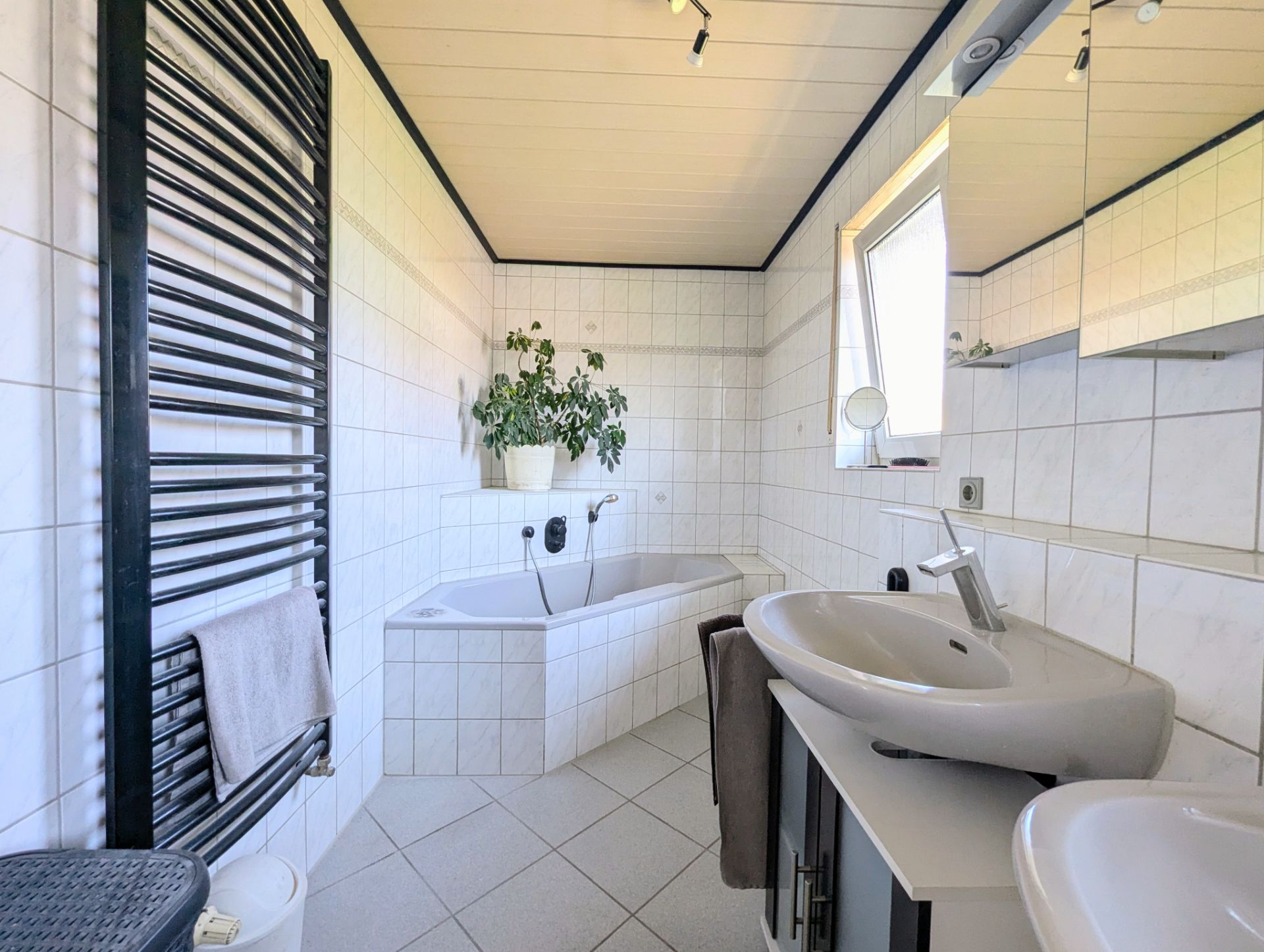 Modernes Badezimmer mit Badewanne, Waschbecken, Handtuchheizkörper und einem Fenster.