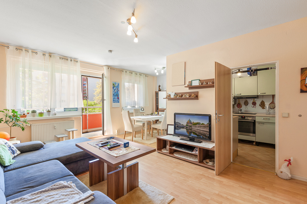 Helles Wohnzimmer mit Sofa, Esstisch, Fernseher und offener Tür zur Küche.