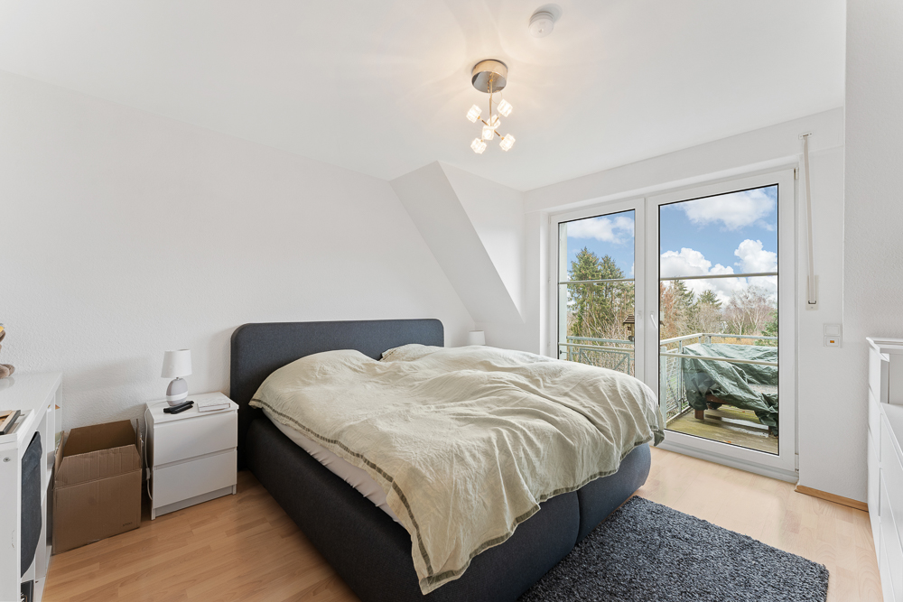Helles Schlafzimmer mit Doppelbett, Nachttischen und großer Fensterfront zum Balkon.