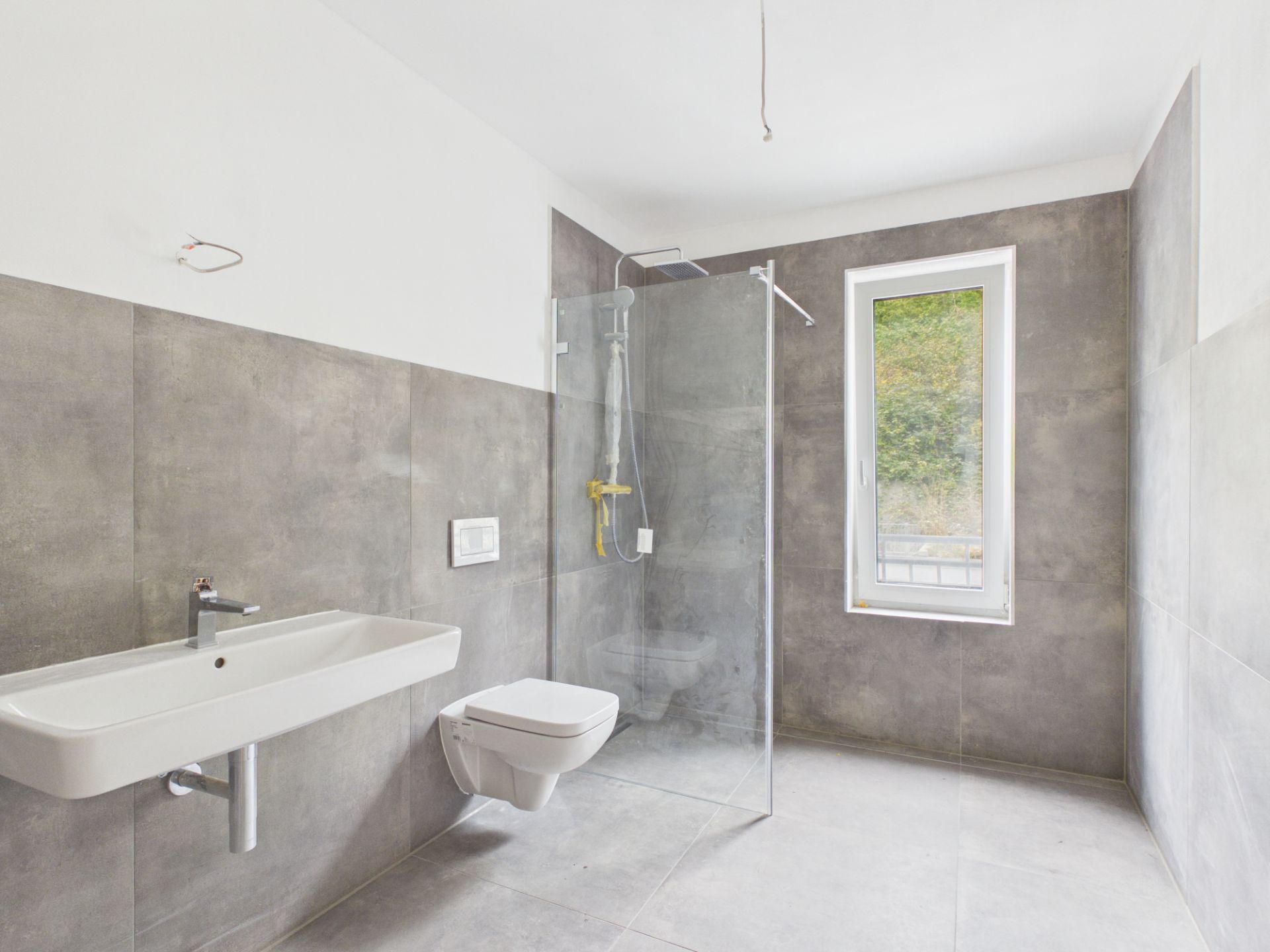 Modernes Badezimmer mit bodengleicher Dusche, Wandwaschbecken, WC und Fenster.