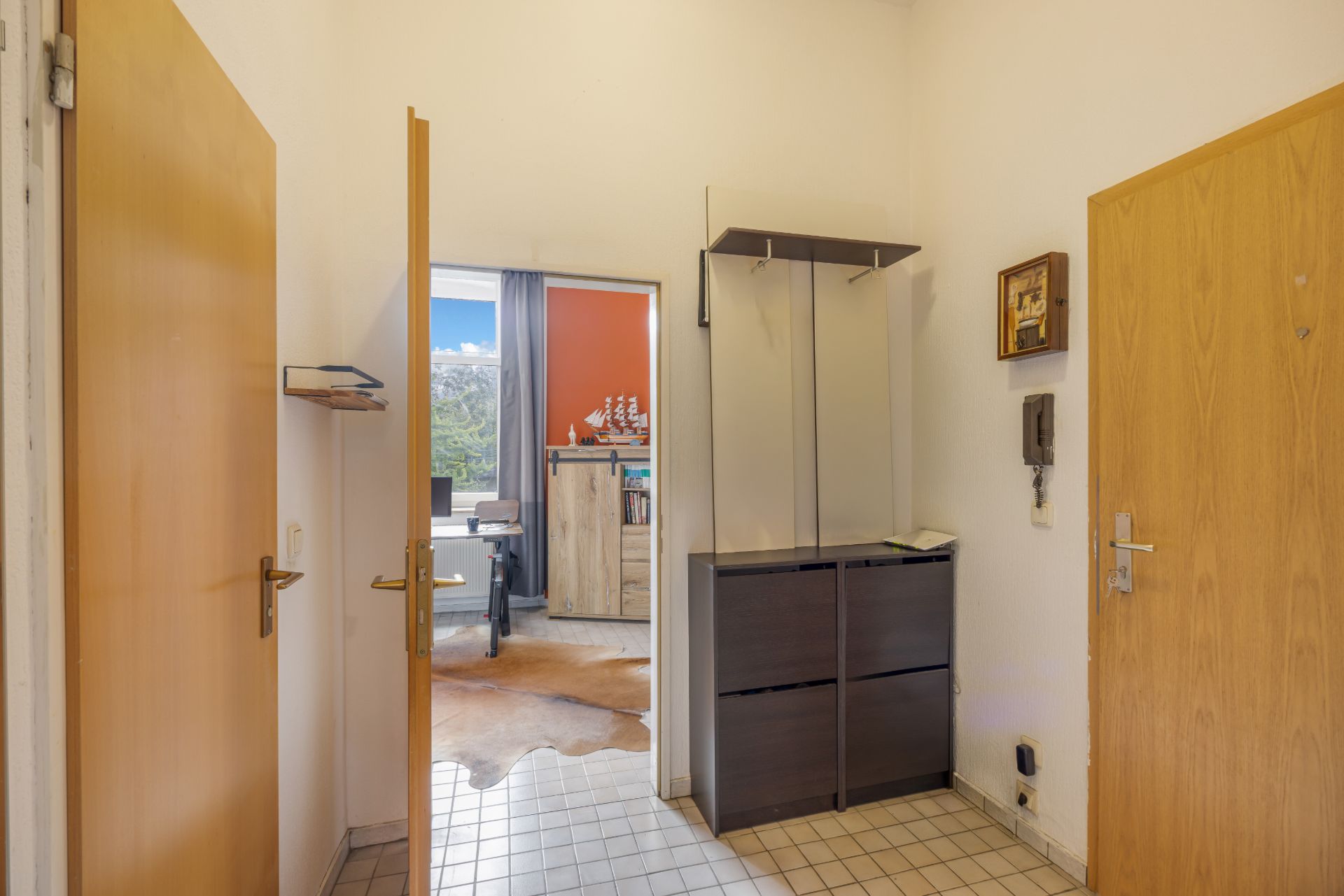 Eingangsbereich einer Wohnung mit Fliesenboden, Garderobe und Blick in ein helles Zimmer.