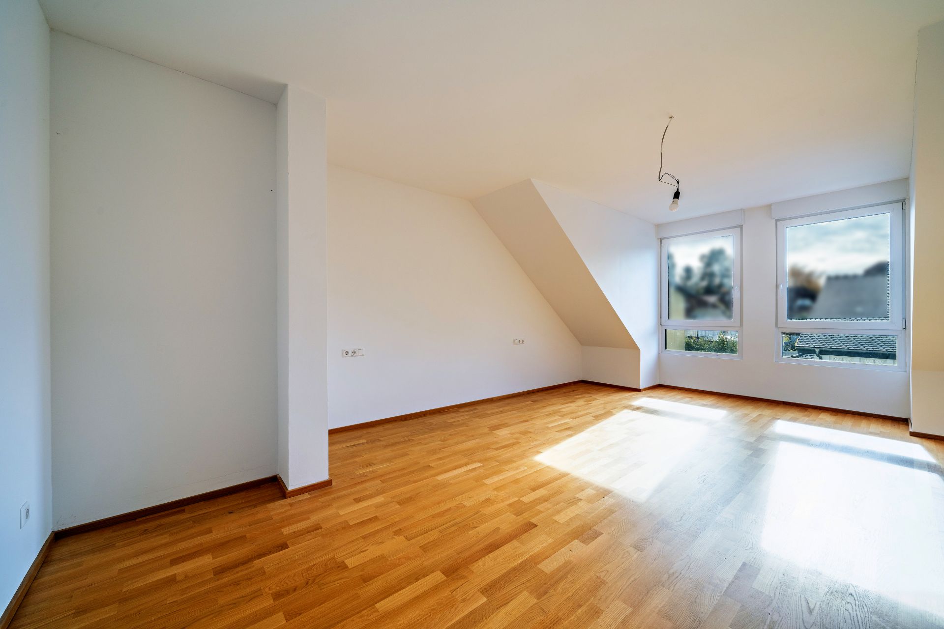 Helles, leeres Zimmer mit Parkettboden, weißen Wänden und drei Fenstern.