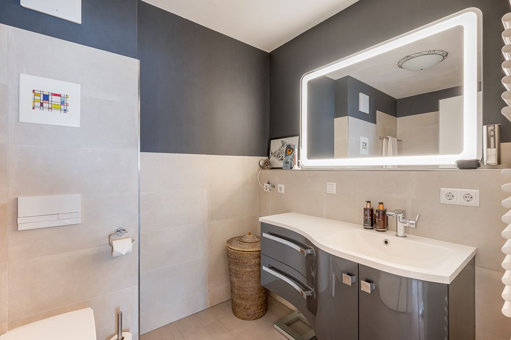 Modernes Badezimmer mit großem Spiegel, Waschbecken und grauen Schränken.