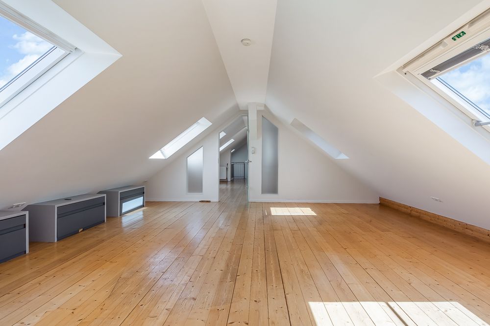 Heller Dachbodenraum mit Holzboden, weißen Wänden und mehreren Dachfenstern.