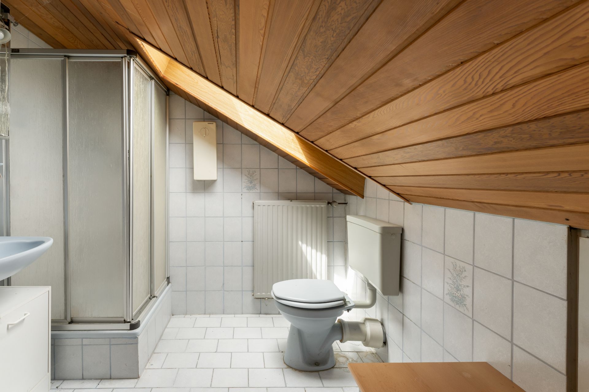 Kleines Bad mit Dusche, Toilette und Waschbecken unter einer Dachschräge mit Holzdecke.
