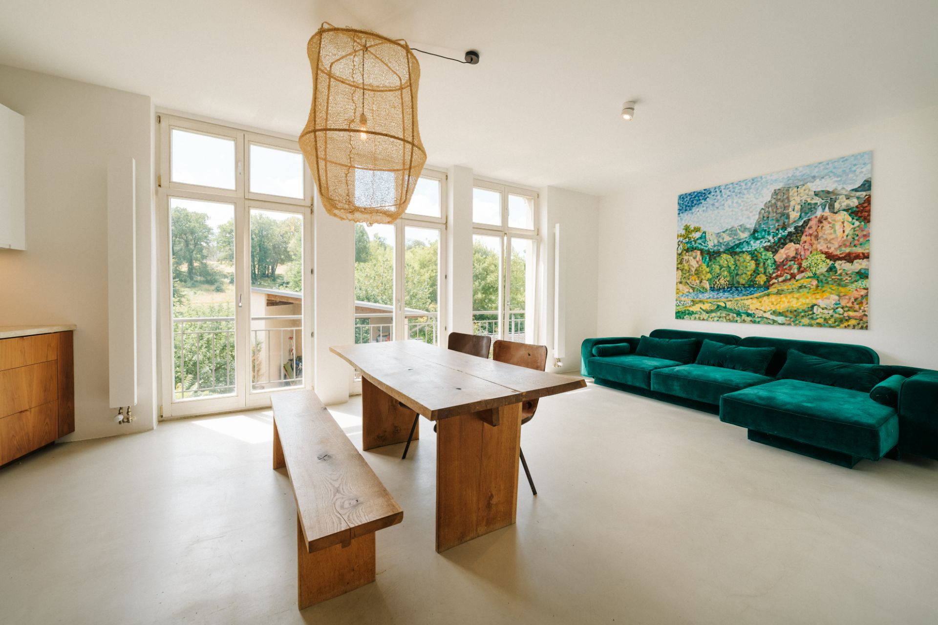 Helles Wohnzimmer mit Holz-Esstisch, grüner Couch und großem Gemälde an der Wand.