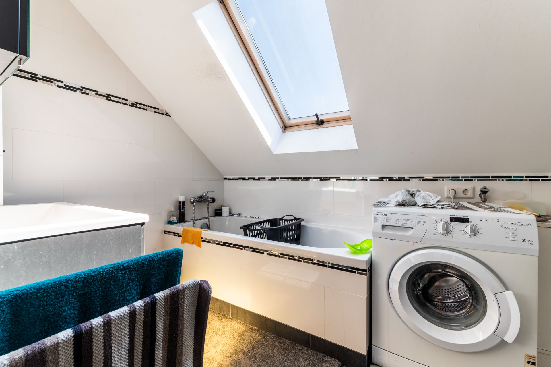 Modernes Badezimmer mit Badewanne, Waschmaschine und Dachfenster unter einer Schräge.