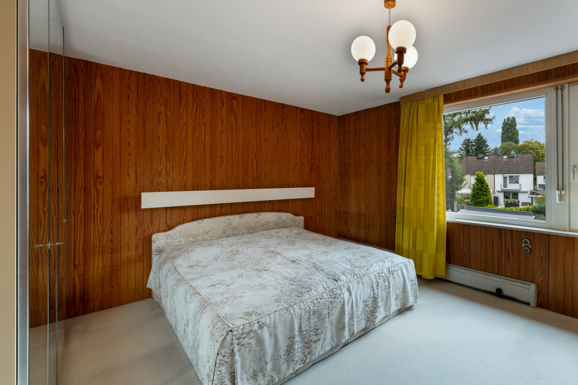 Schlafzimmer mit Doppelbett, Holzvertäfelung an den Wänden und großem Fenster mit gelbem Vorhang.