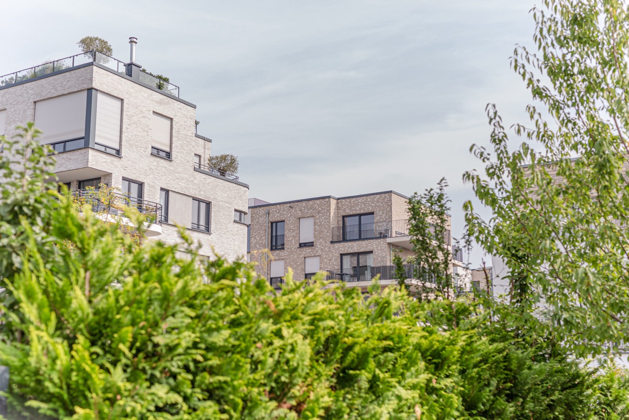 Moderne Wohngebäude mit Balkonen, umgeben von grünen Bäumen und Sträuchern.