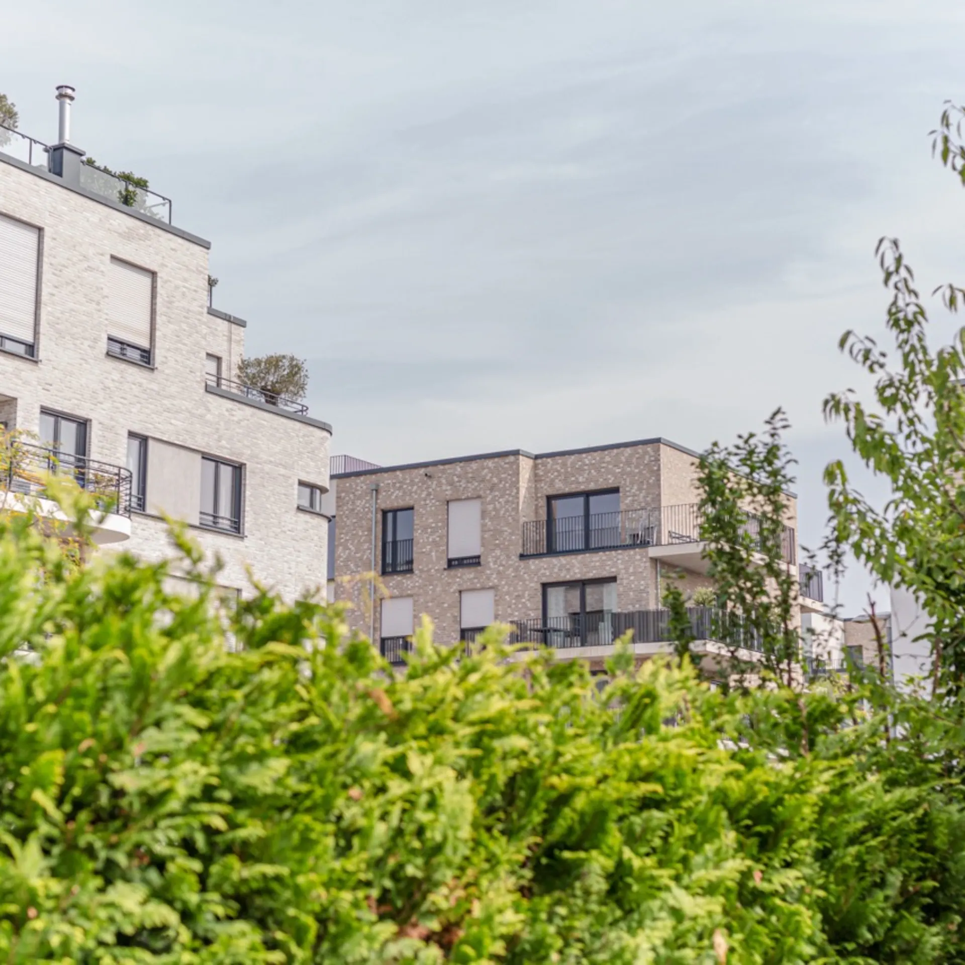 Moderne Wohngebäude mit Balkonen, umgeben von grünen Bäumen und Sträuchern.