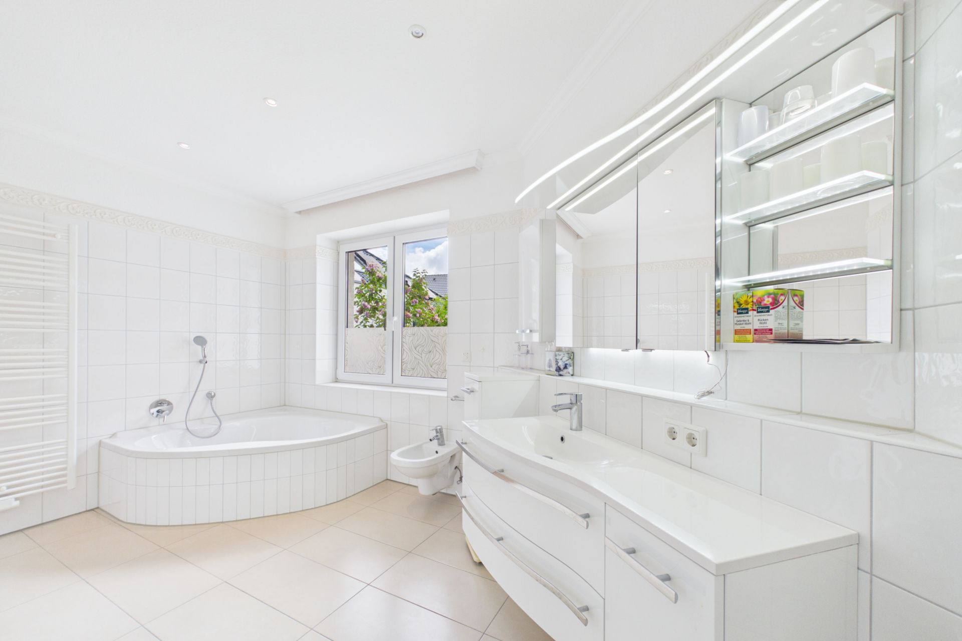 Helles Badezimmer mit Eckbadewanne, Doppelwaschbecken, Bidet und großem Fenster.