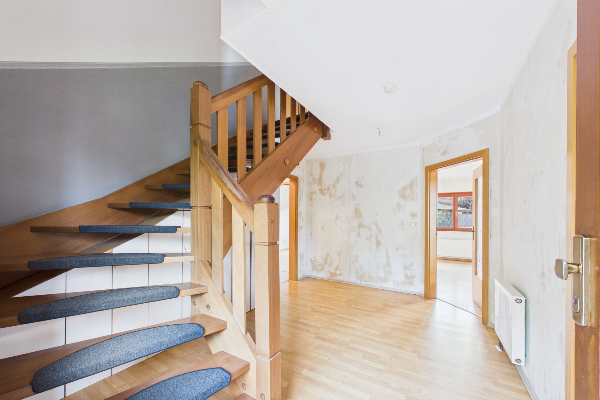 Heller Flur mit Holztreppe und zwei offenen Türen zu weiteren Räumen.