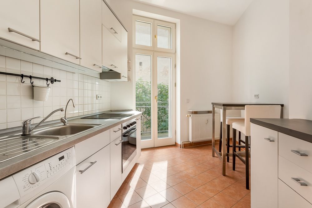 Helle Küche mit weißen Schränken, Esstisch, Stühlen und Zugang zu einem Balkon.